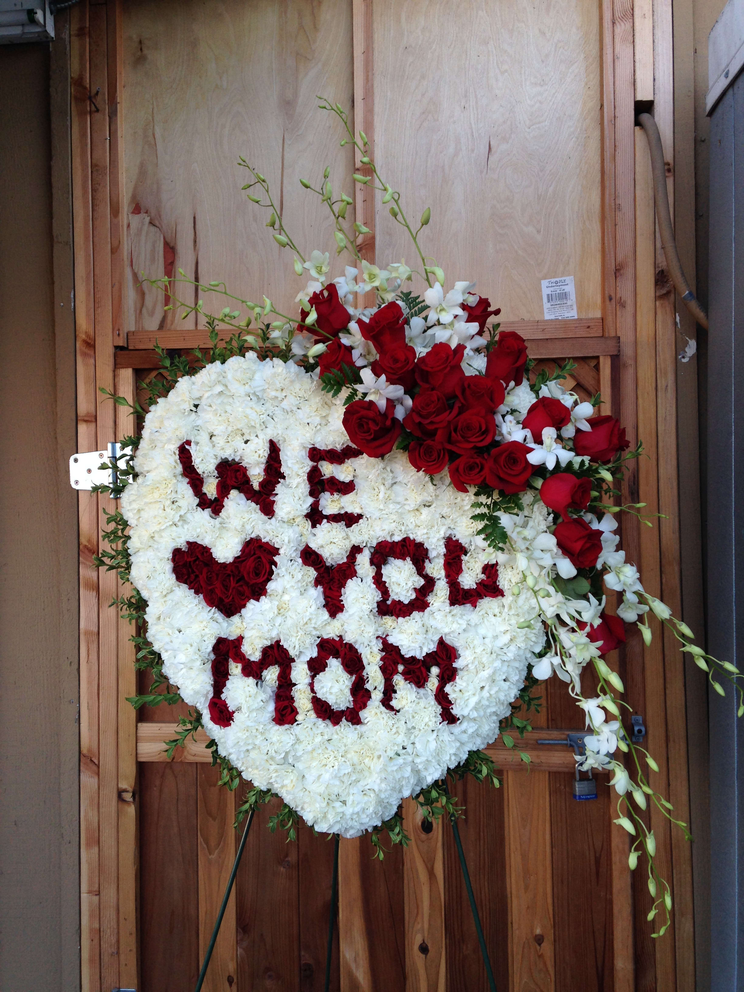 Heart-shaped floral tribute with red roses and white flowers spelling "WE WILL MISS YOU"