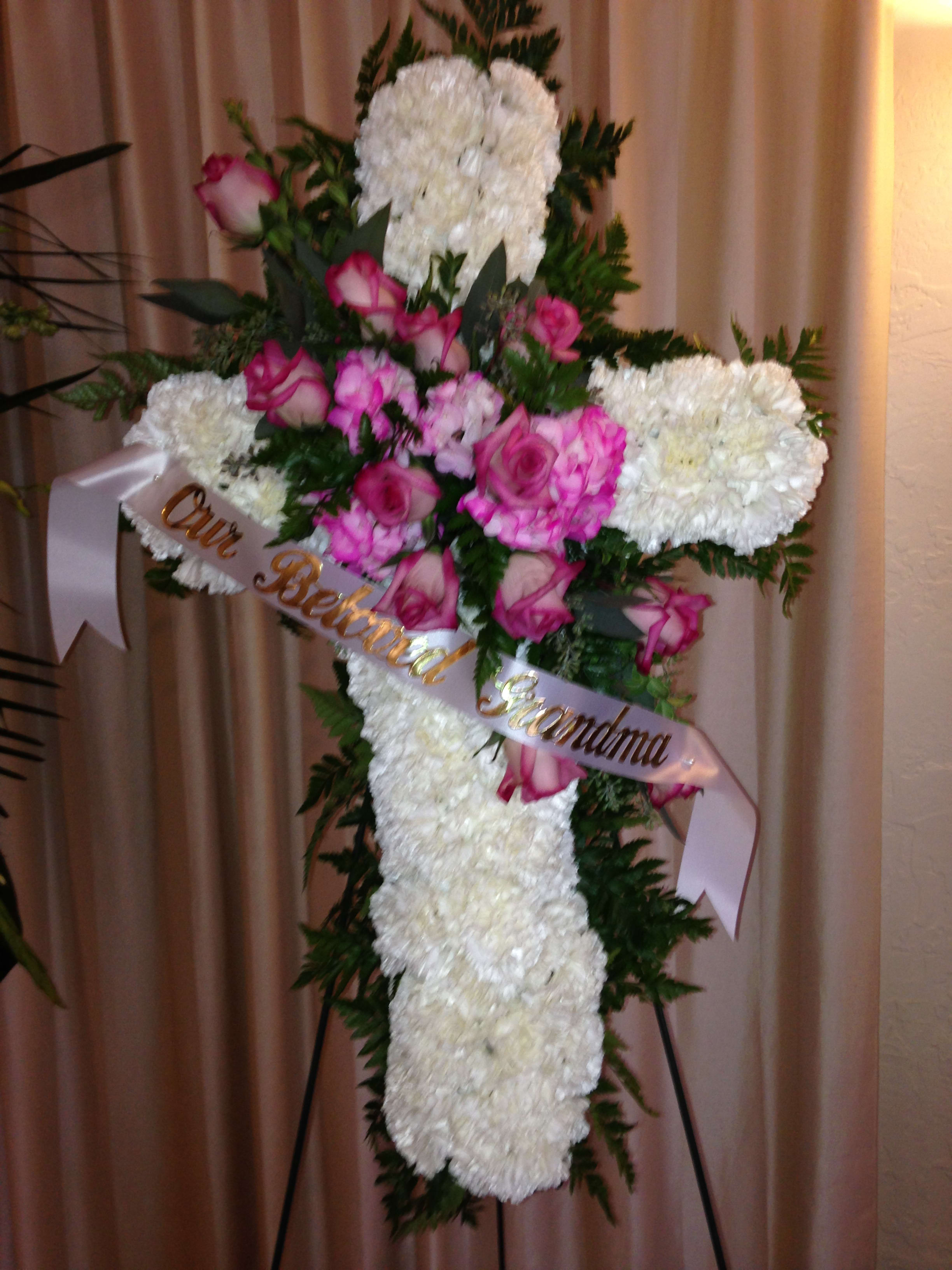 White floral cross with pink roses and ribbon on an easel