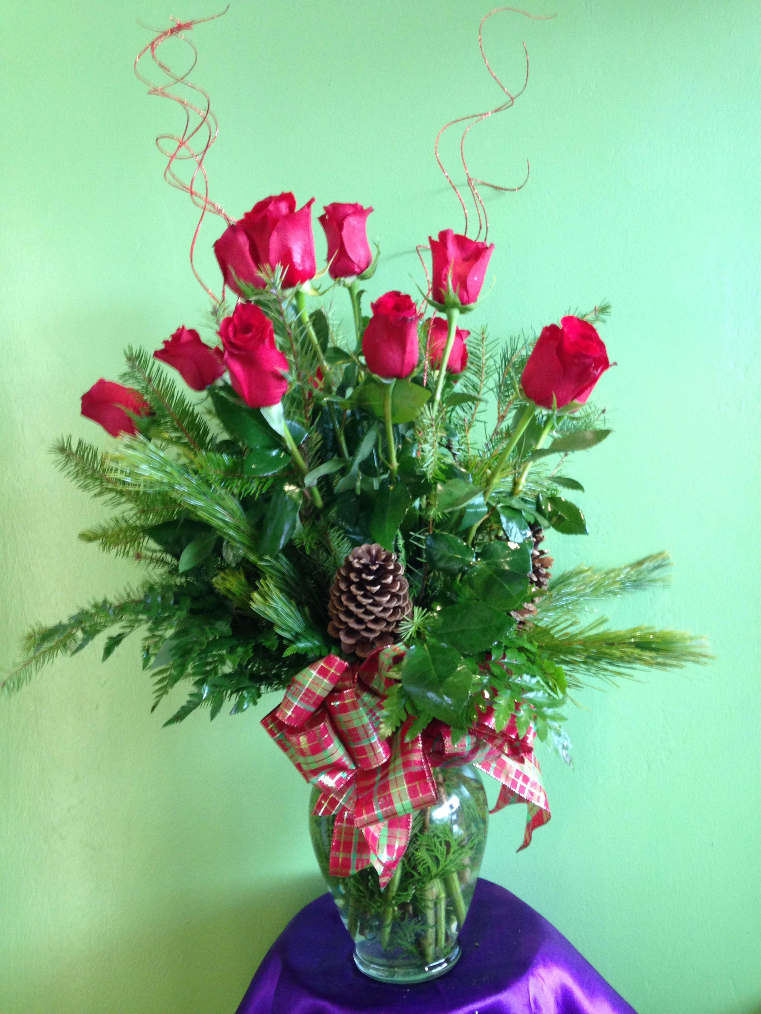Red roses arranged in a glass vase with pinecones and plaid ribbon