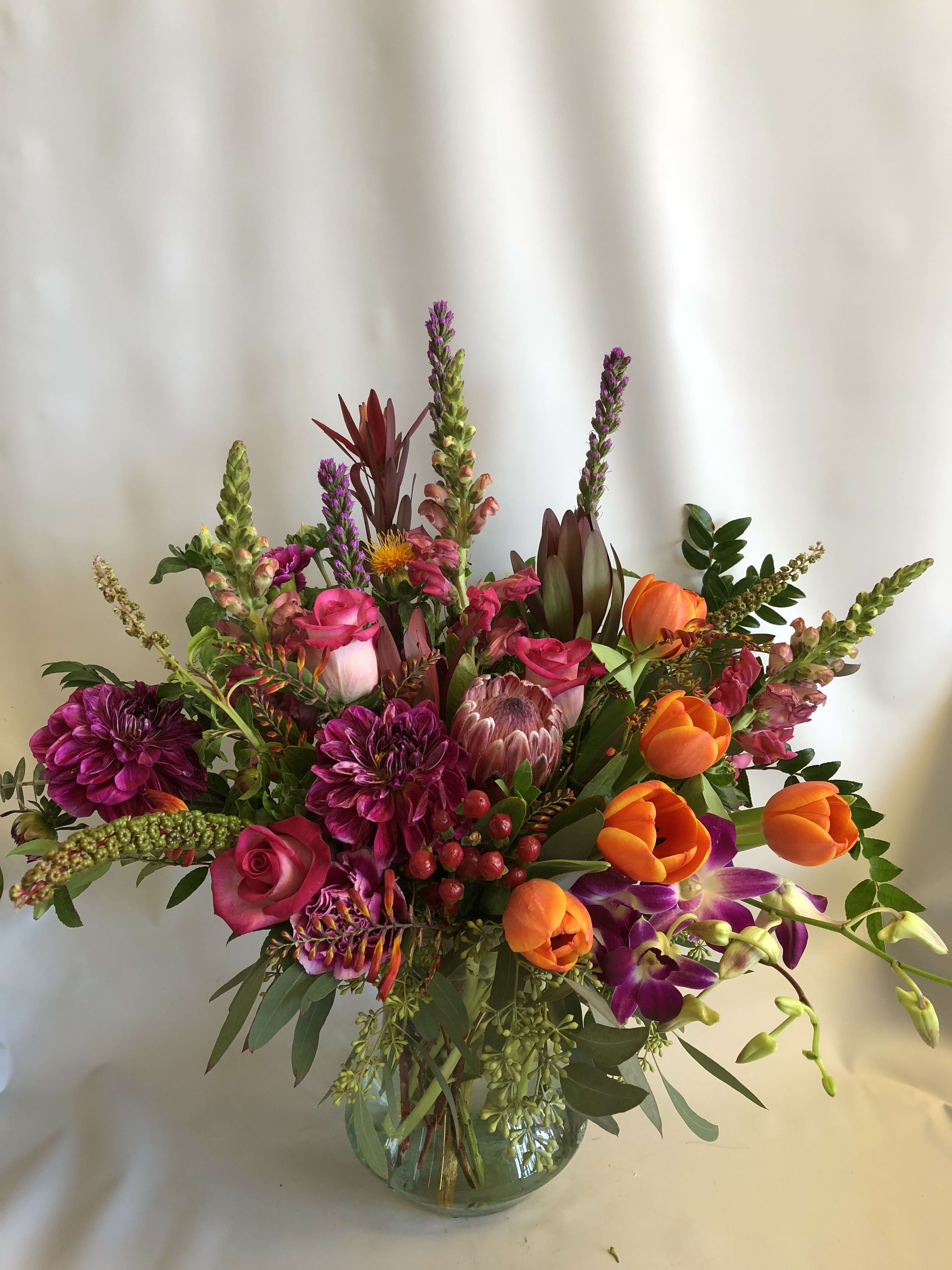 Mixed bouquet of pink, orange, and purple flowers in a glass vase