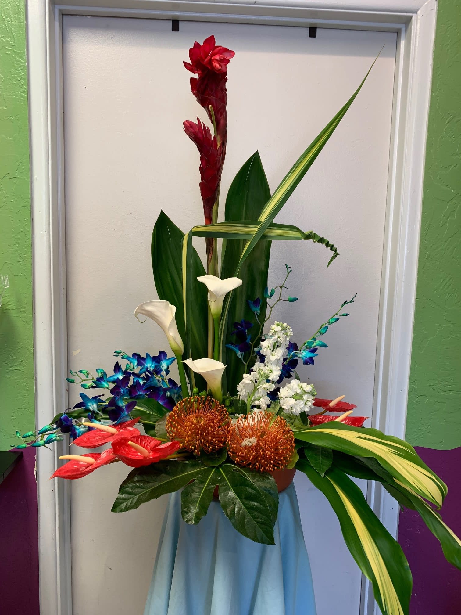 Tropical floral arrangement with red blooms, white calla lilies, and blue orchids