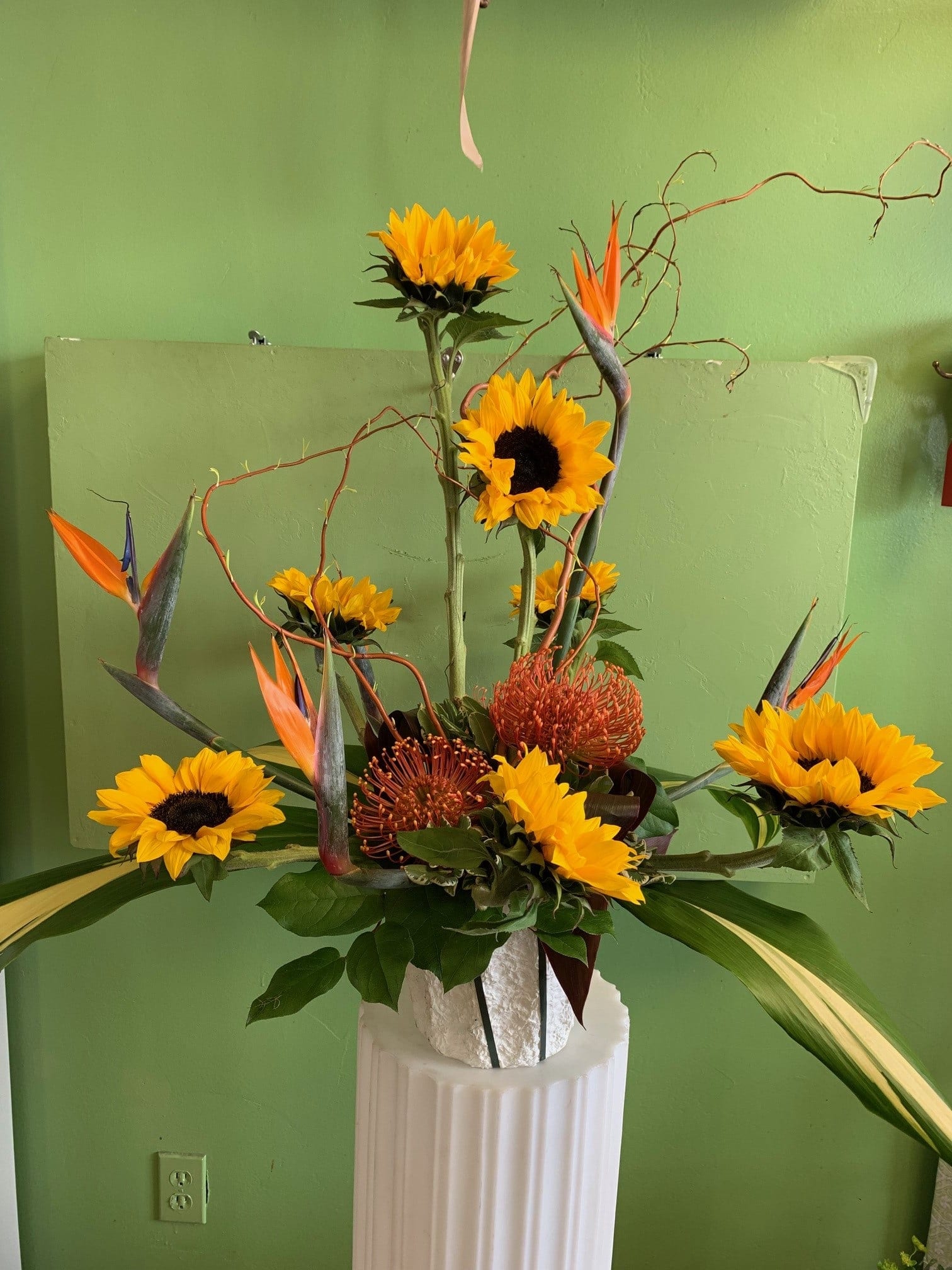 Tall floral arrangement with sunflowers and orange bird-of-paradise in a white vase