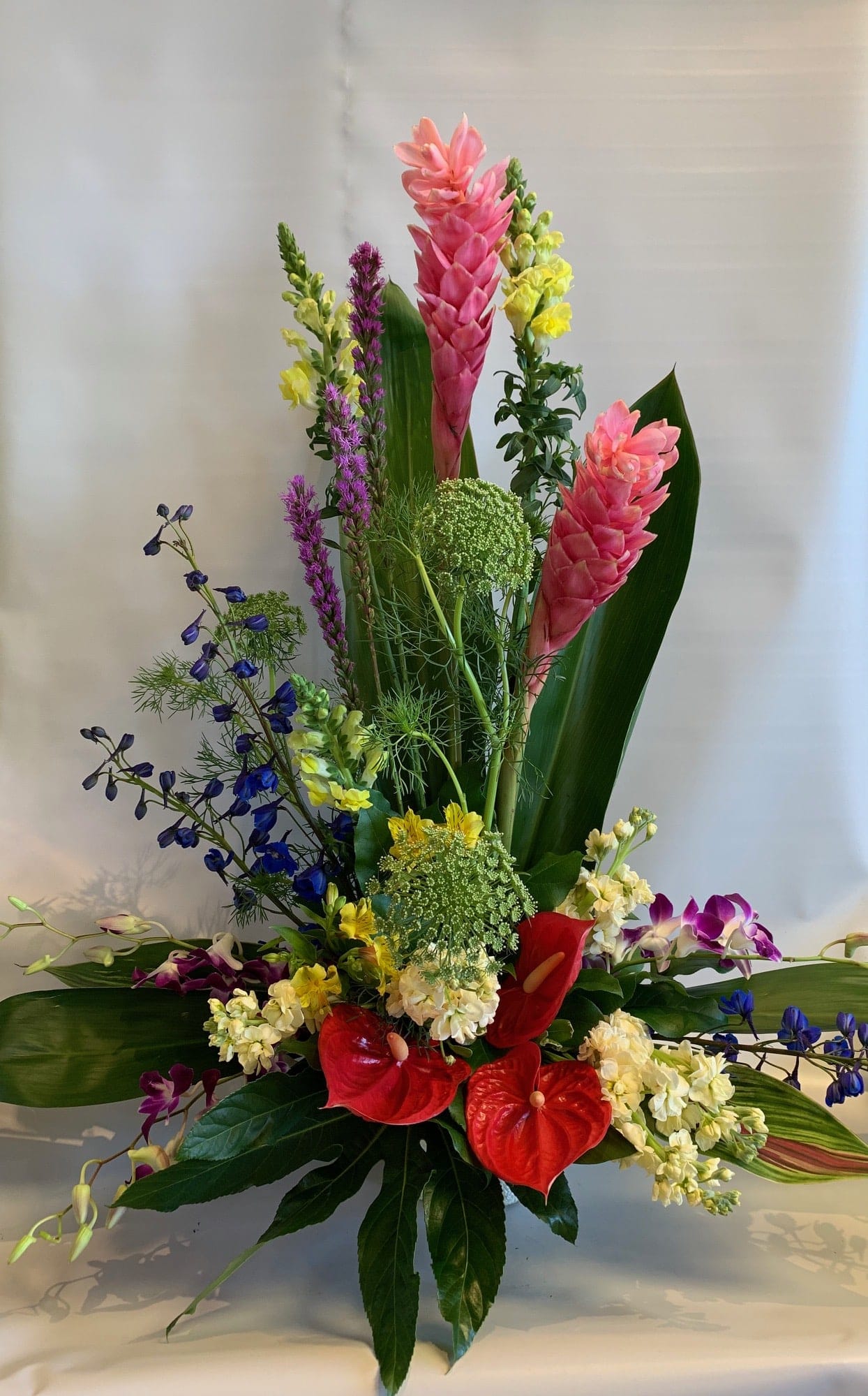 Tall tropical arrangement with pink ginger, red anthuriums, and purple orchids