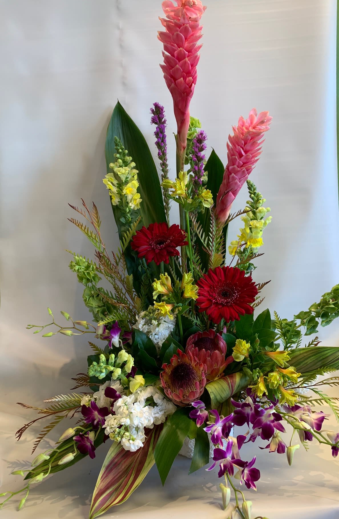 Tall tropical flower arrangement with pink ginger, red gerberas, and purple orchids
