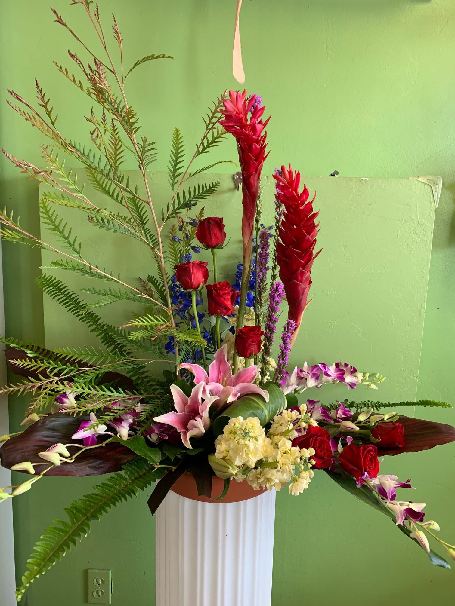 Tall floral arrangement with red roses, pink lilies, and purple orchids in a vase
