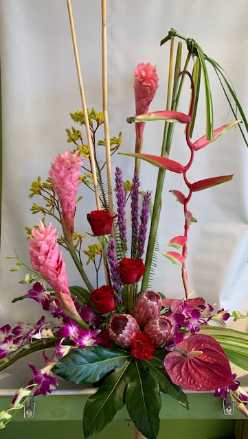 Tall tropical floral arrangement with pink and red blooms in a container