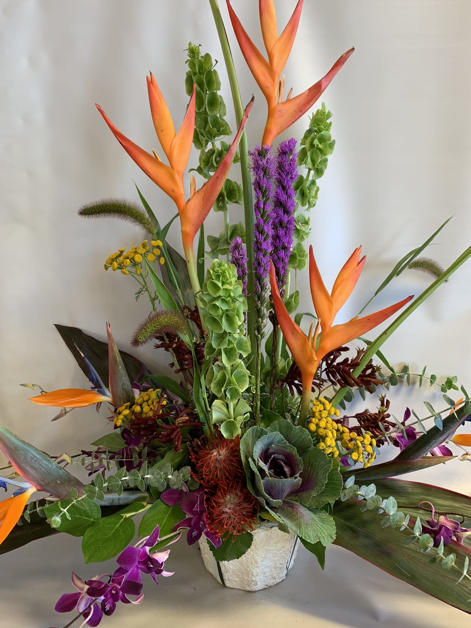 Tropical arrangement with orange bird-of-paradise and purple orchids in a white vase