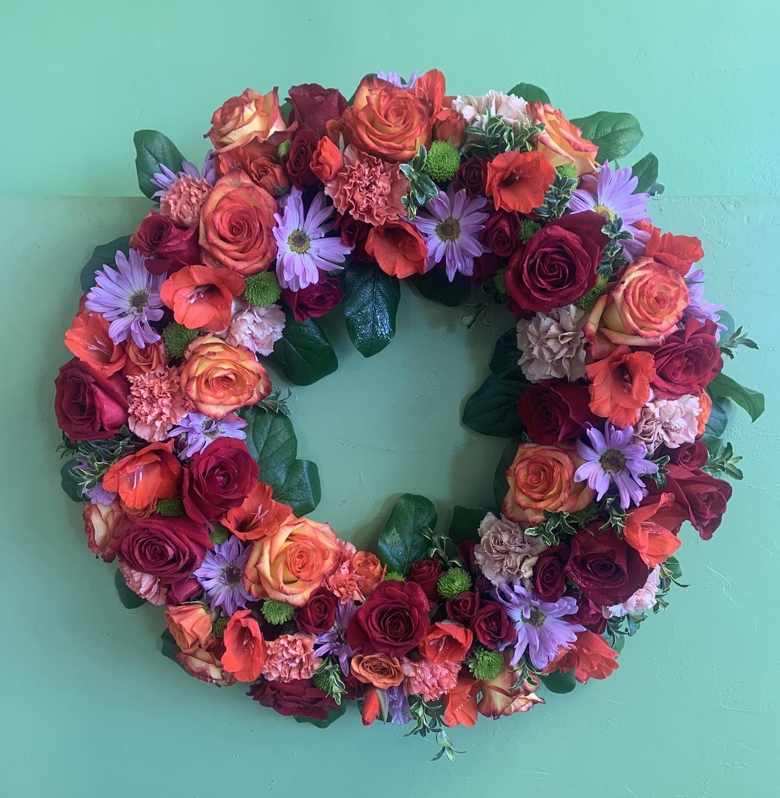 Circular floral wreath with roses, daisies, and carnations on a green background