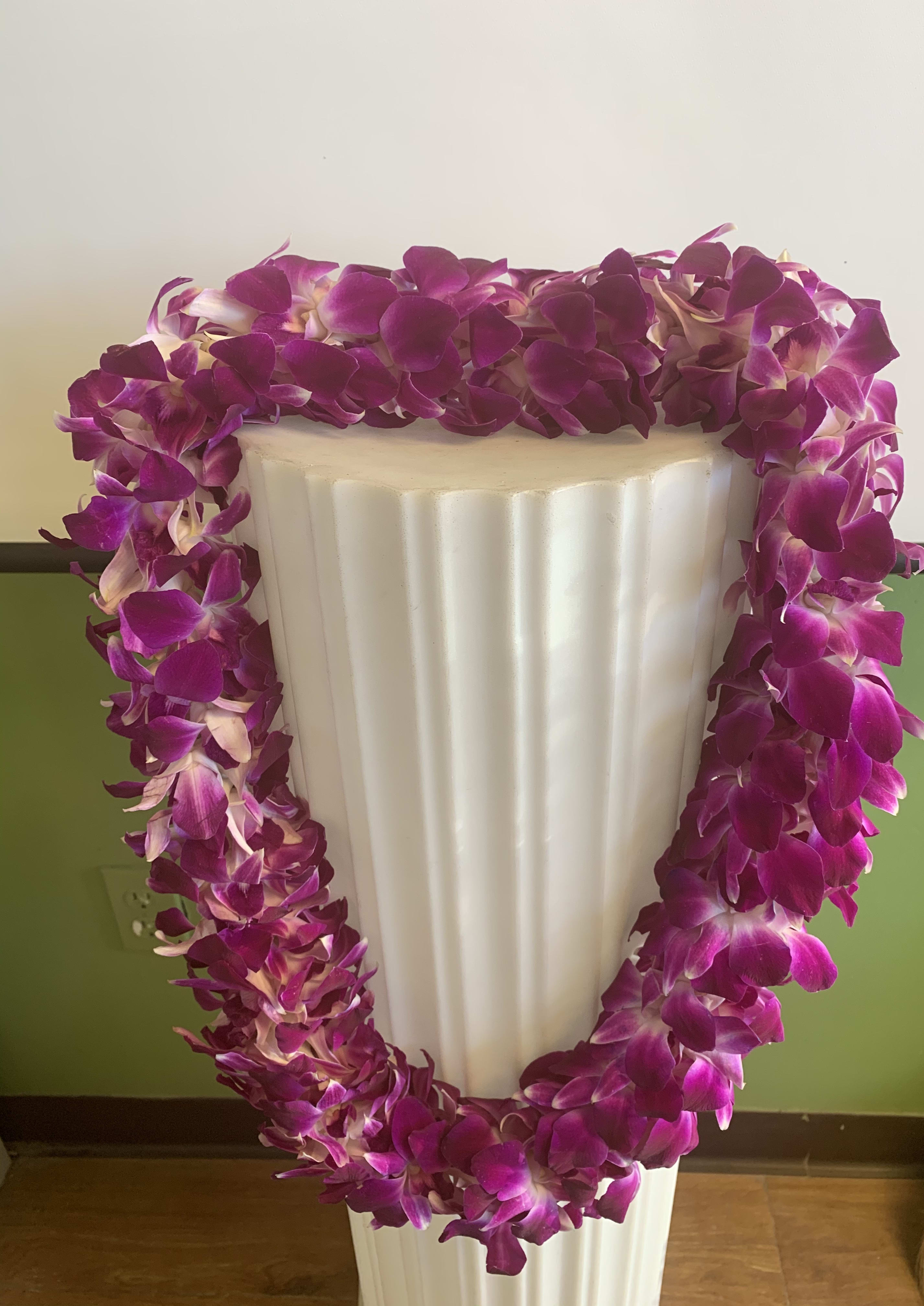 Purple orchid lei draped over a white pedestal vase