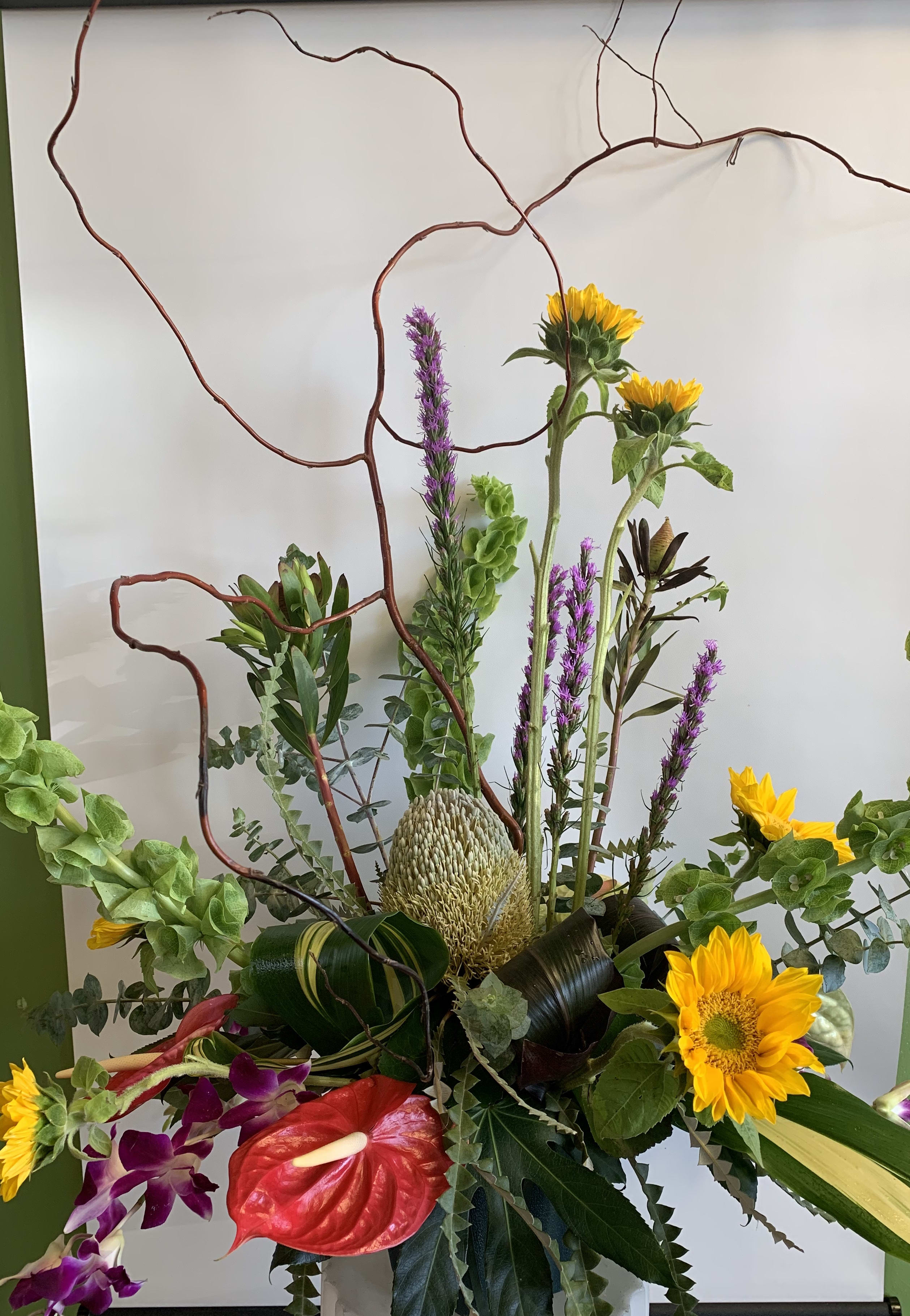 Tall floral arrangement with sunflowers, orchids, and a red anthurium