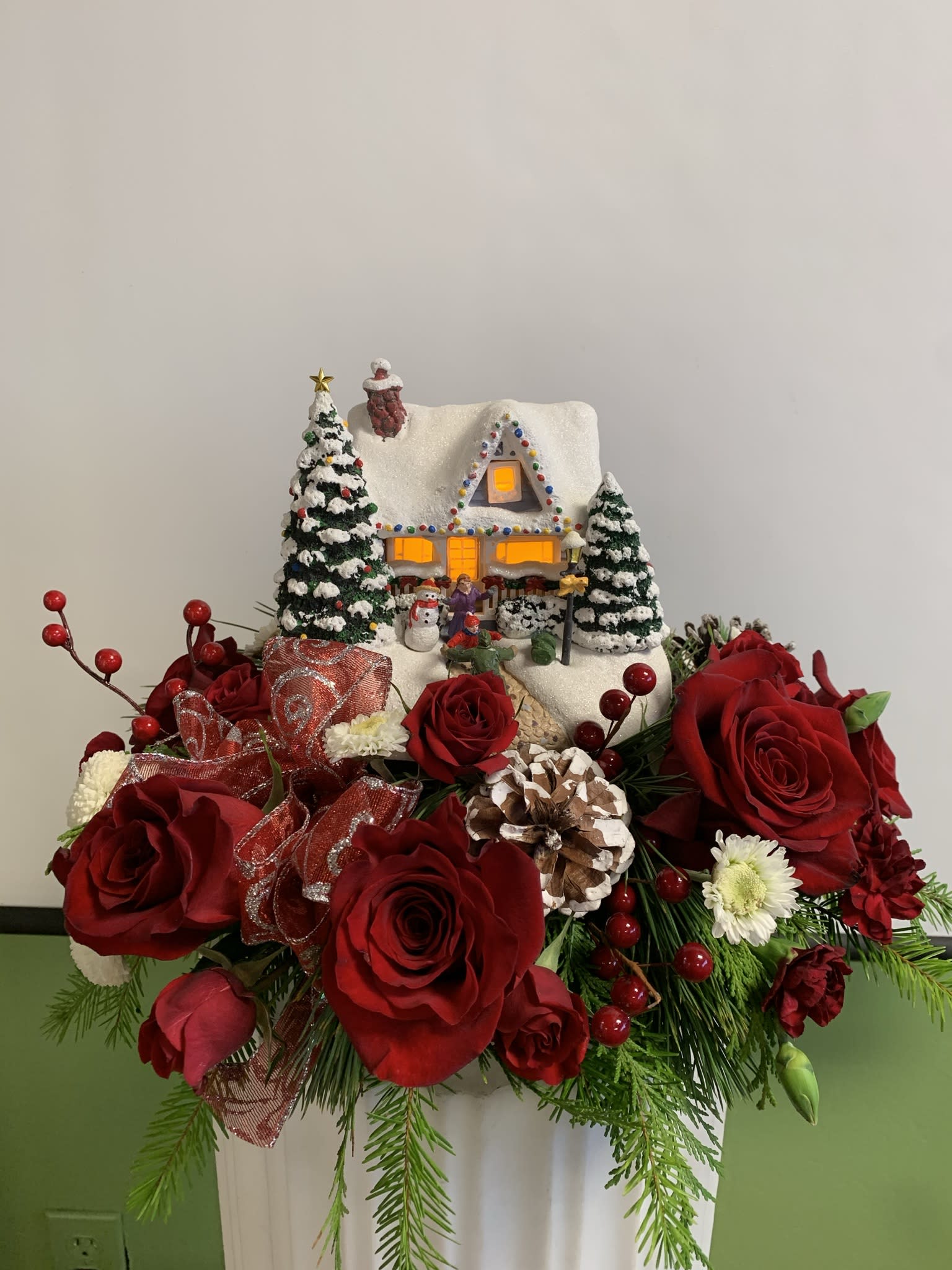 Christmas floral arrangement with red roses and a snowy house decoration
