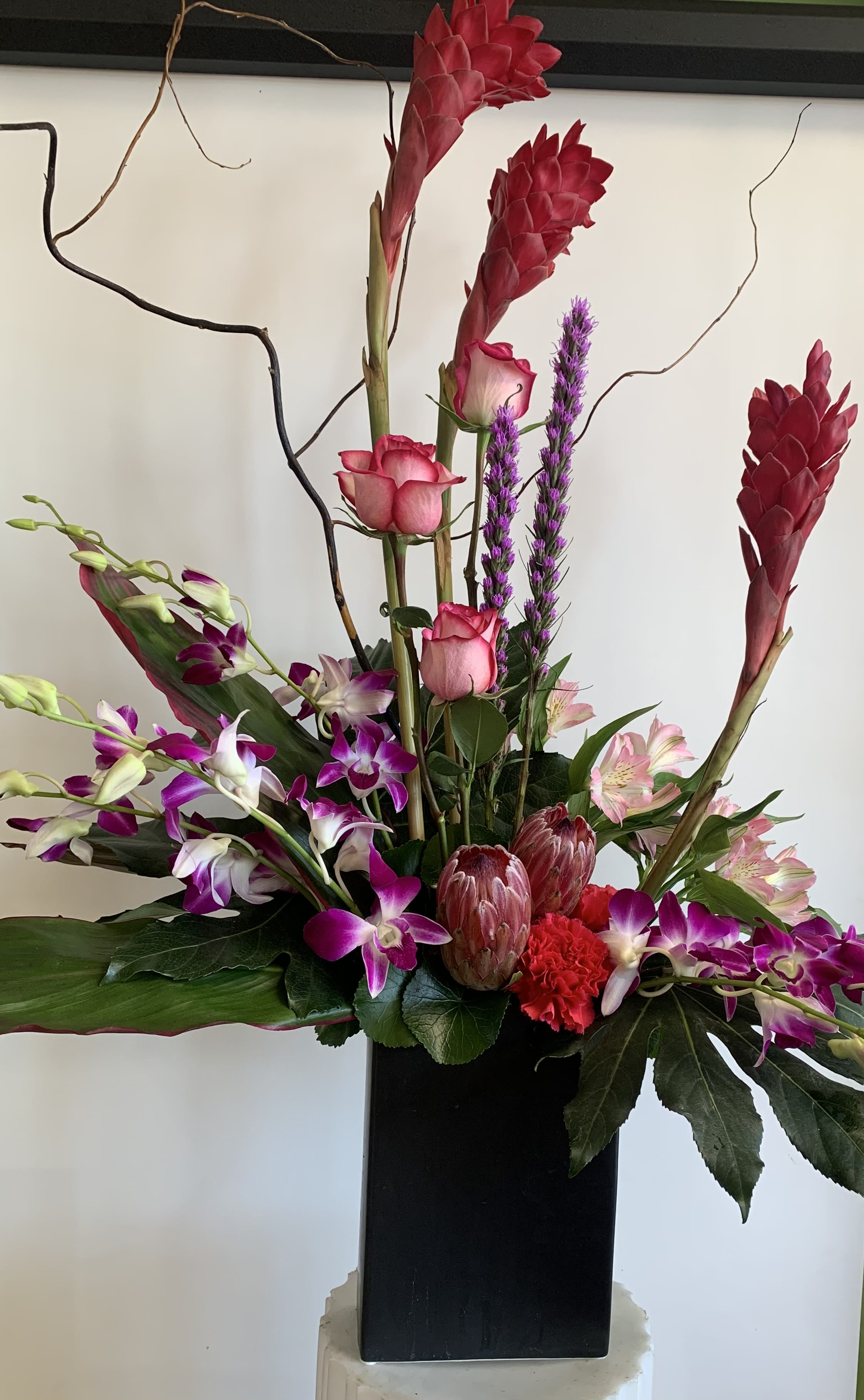 Tall floral arrangement with pink roses, purple orchids, and red tropical blooms in a black vase