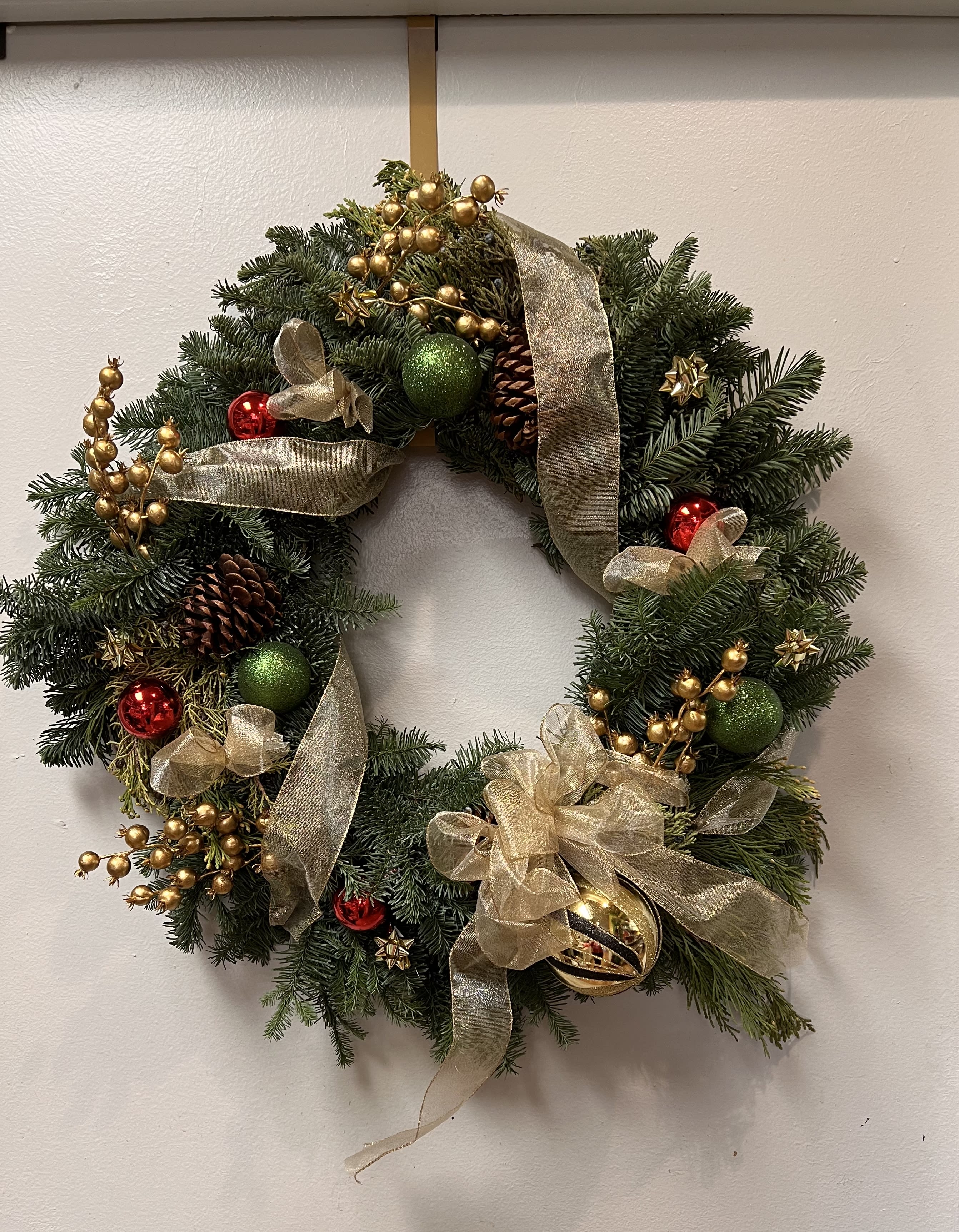 Christmas wreath with gold ribbon, ornaments, and pinecones