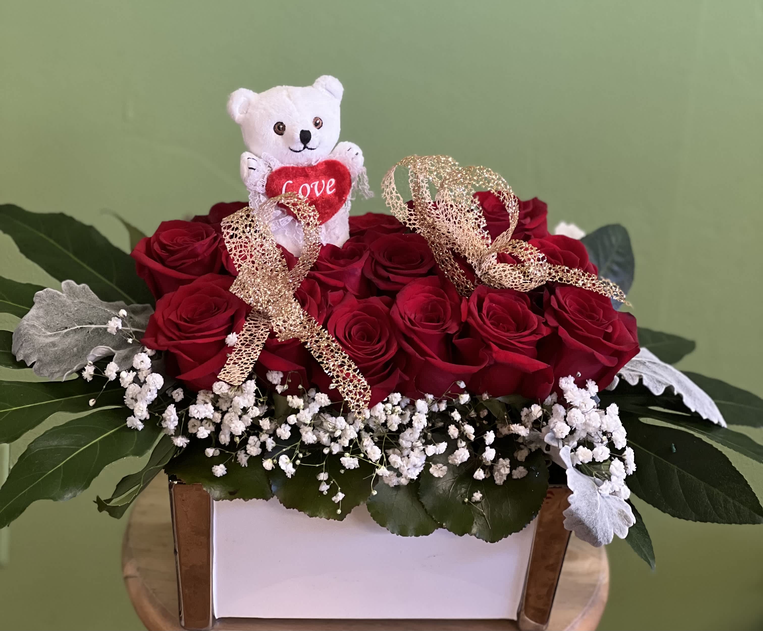 Red roses arranged in a white box with a small teddy bear and ribbon