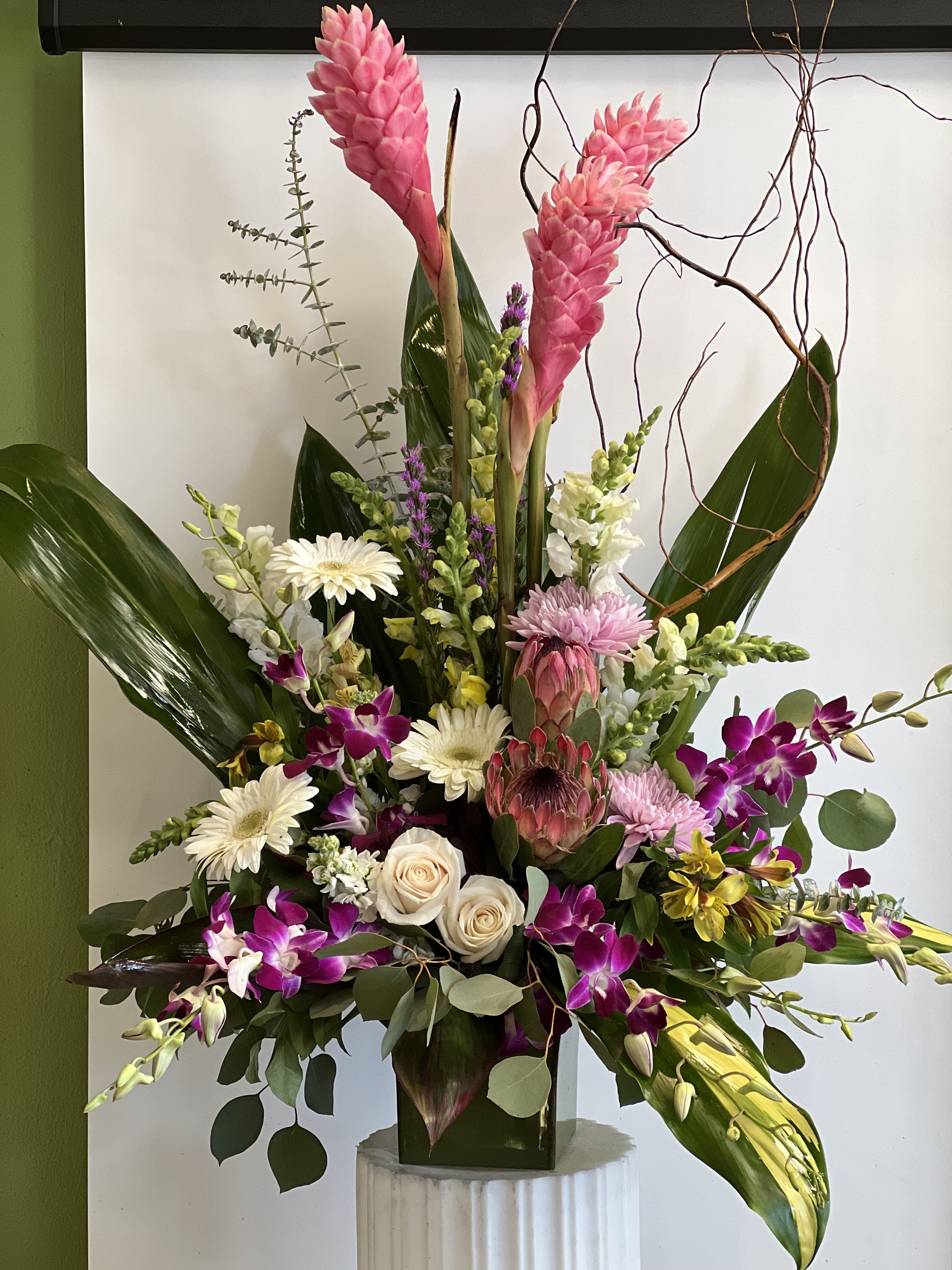 Tall mixed floral arrangement with pink tropical blooms and orchids in a vase