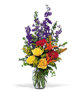 Tall mixed bouquet in a clear glass vase with yellow roses and purple flowers