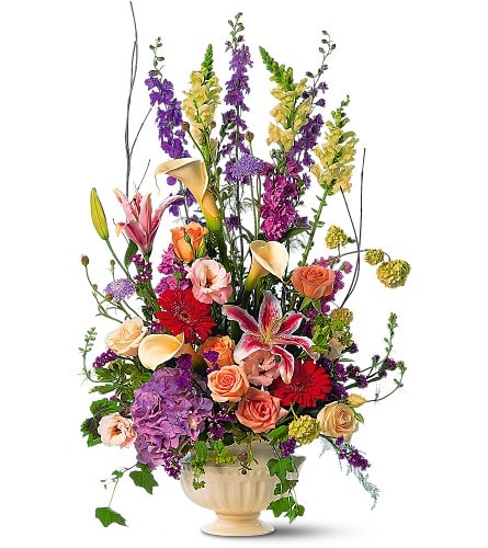Tall mixed bouquet with roses, lilies, calla lilies, and purple blooms in a cream vase
