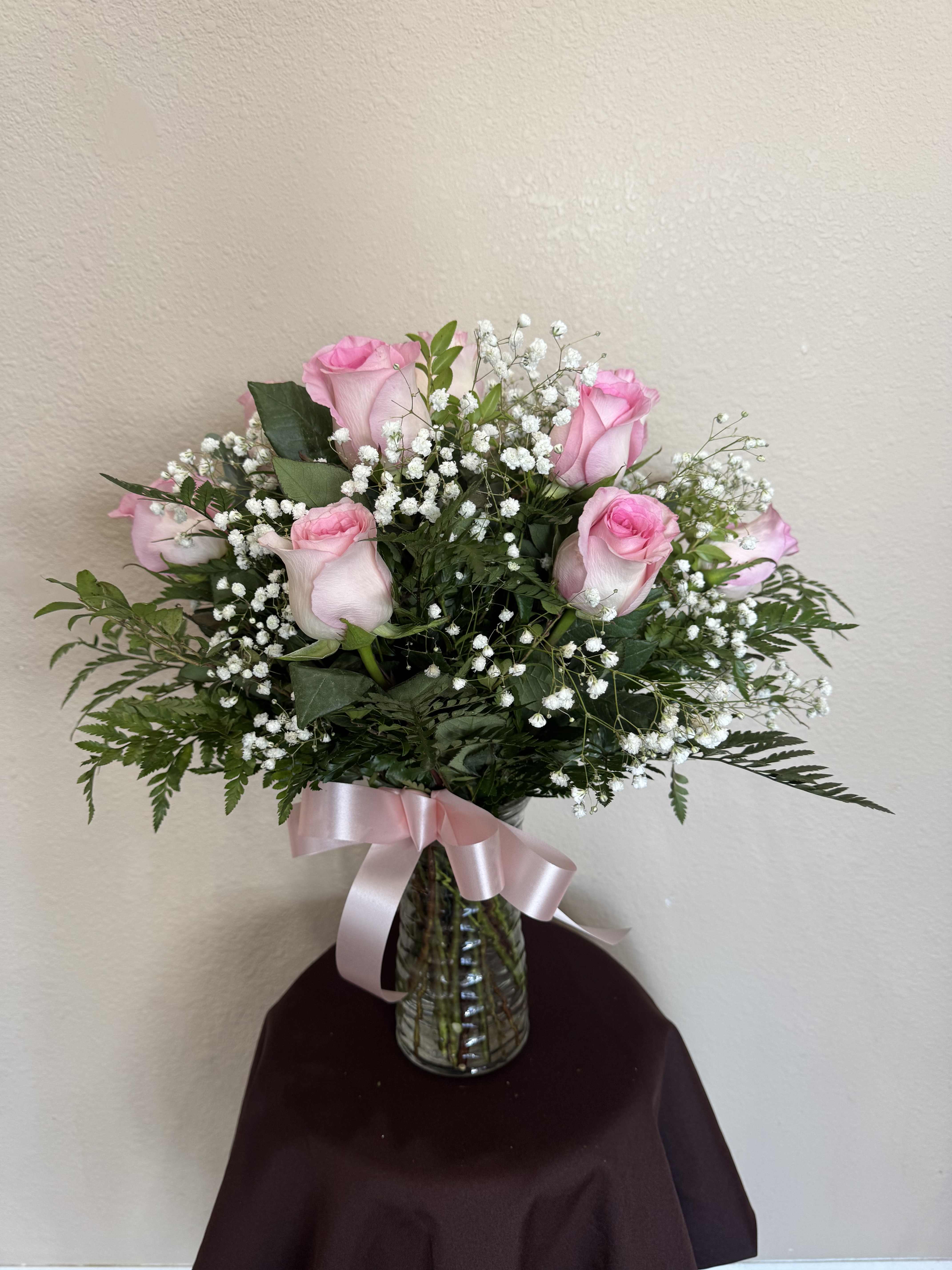 Pink roses and baby's breath in a glass vase with a pink ribbon