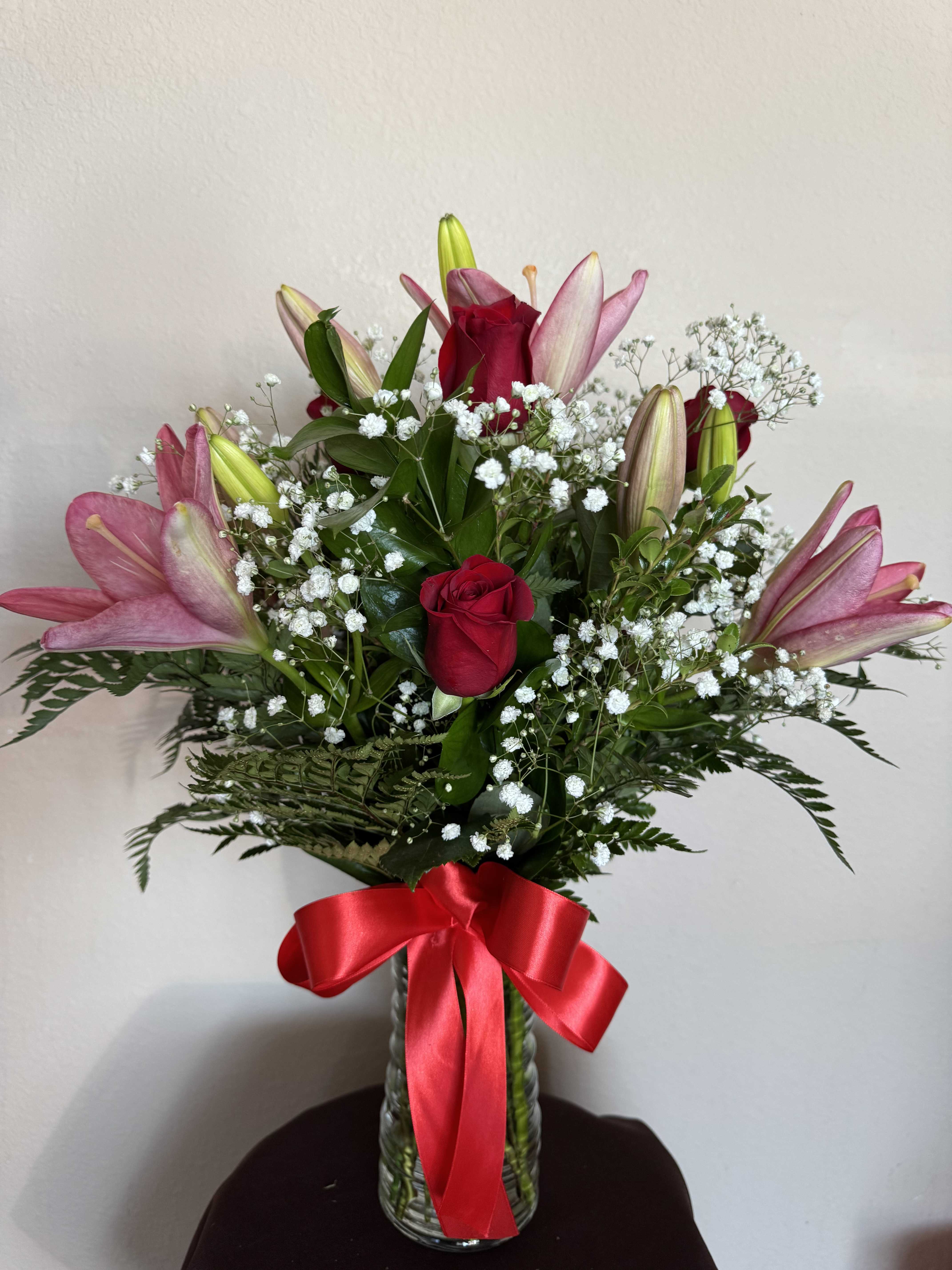 Pink lilies and red roses in a glass vase with a red ribbon