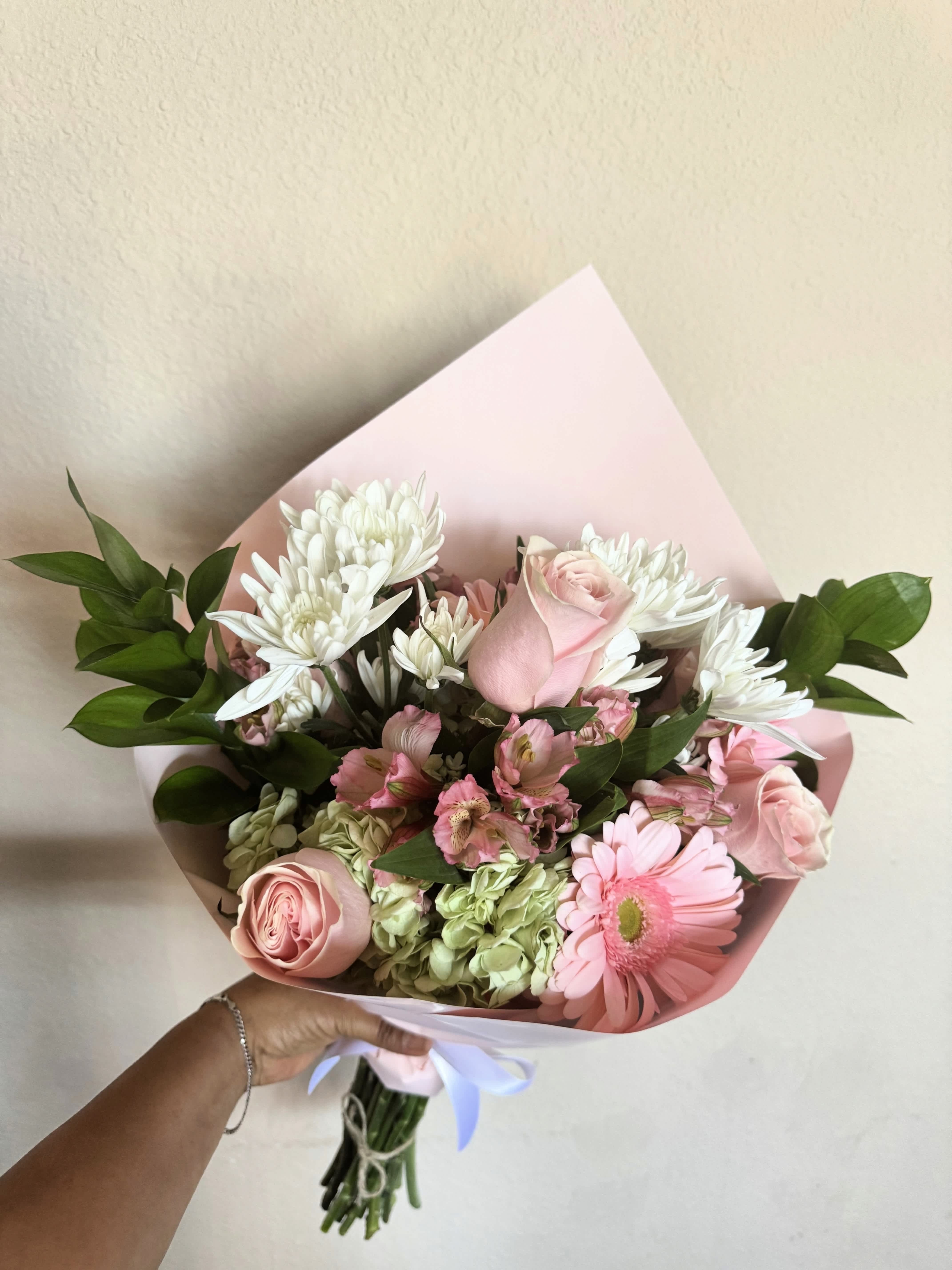 Pink and white bouquet with roses, daisies, and hydrangeas wrapped in pastel paper