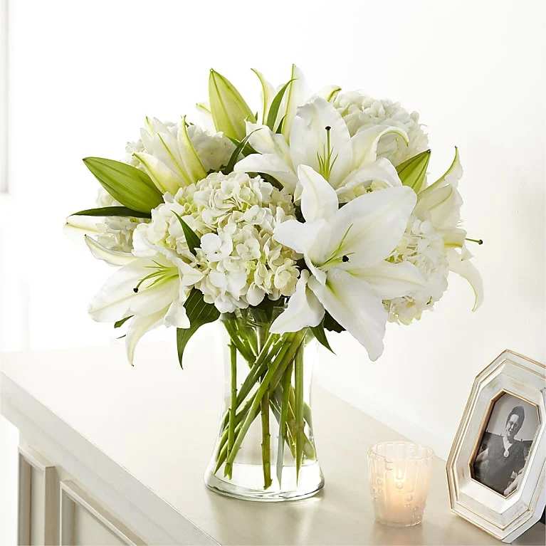 White lilies and hydrangeas arranged in a clear glass vase