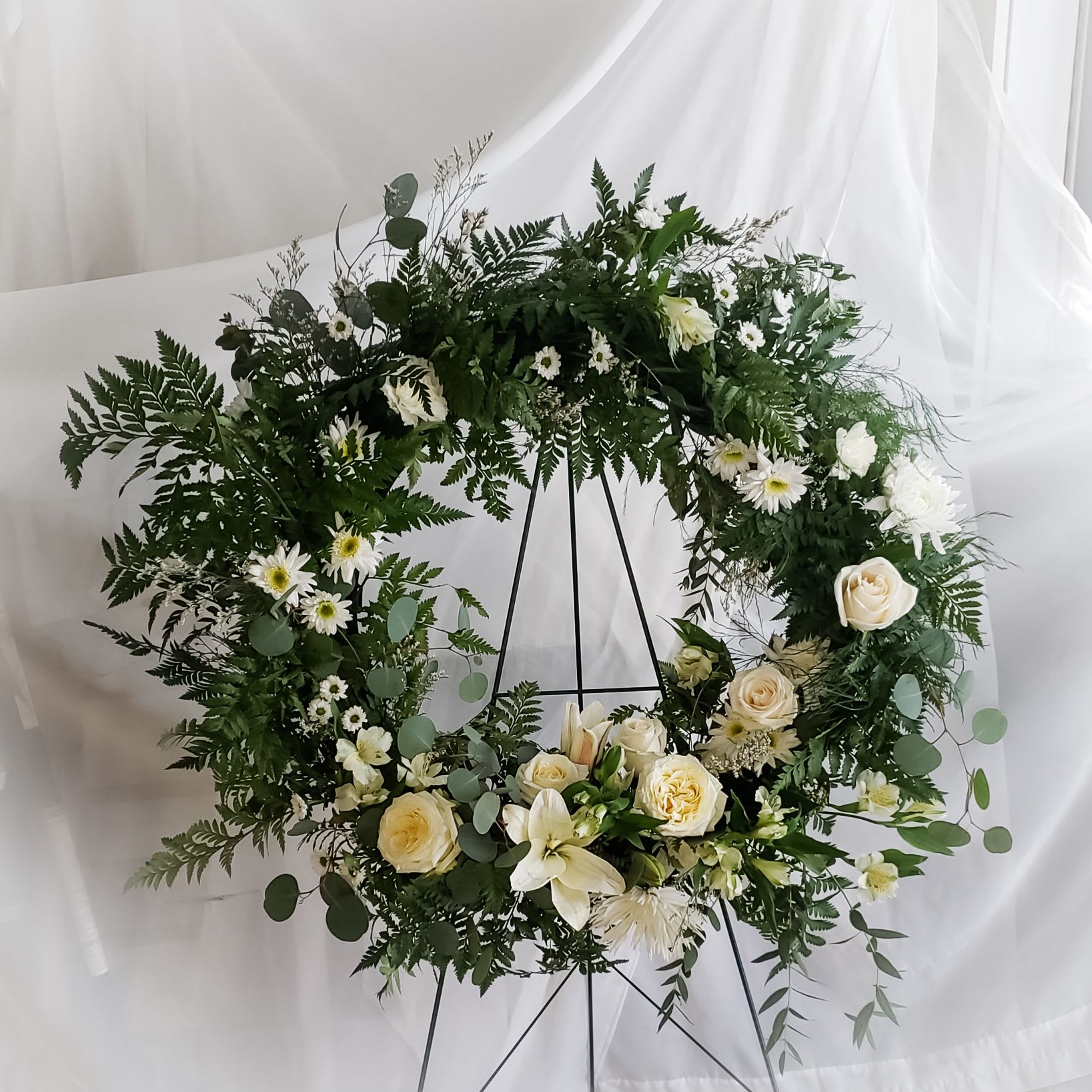 White floral wreath with roses and daisies on a black stand