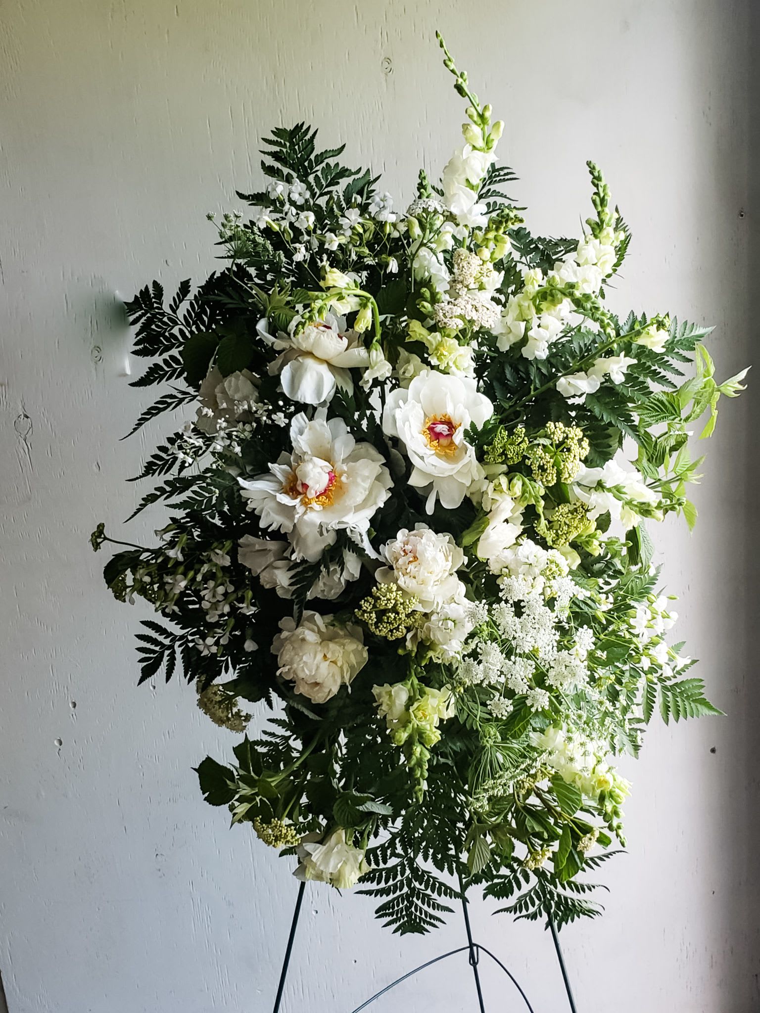 Large white floral standing spray with mixed greenery on an easel
