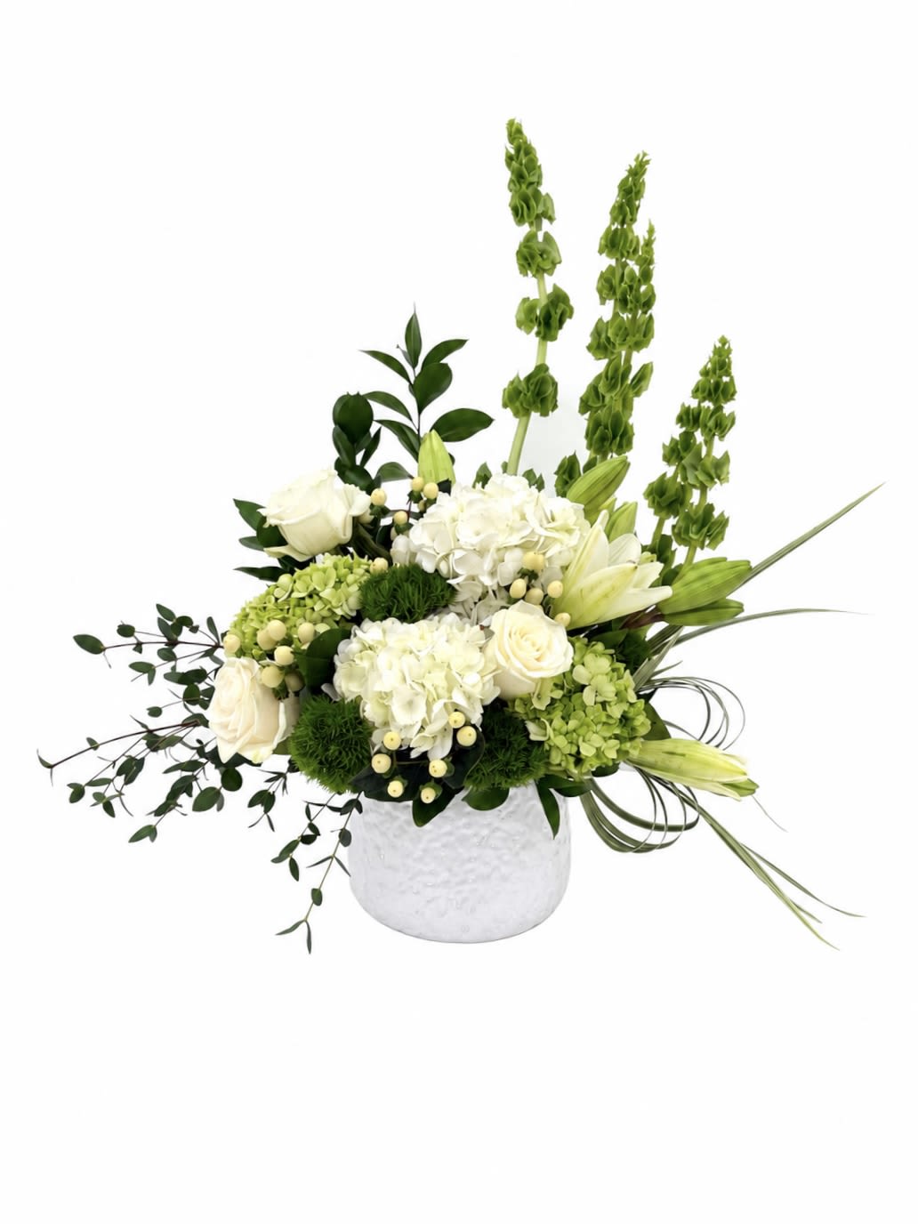Pure Elegance  - A graceful and elegant arrangement featuring white roses, hydrangeas, lilies, green bells of Ireland, and lush greenery in a modern white ceramic vase. Designed with fresh textures and natural movement, this sophisticated centerpiece brings timeless beauty and serenity to any home, celebration, or special occasion.