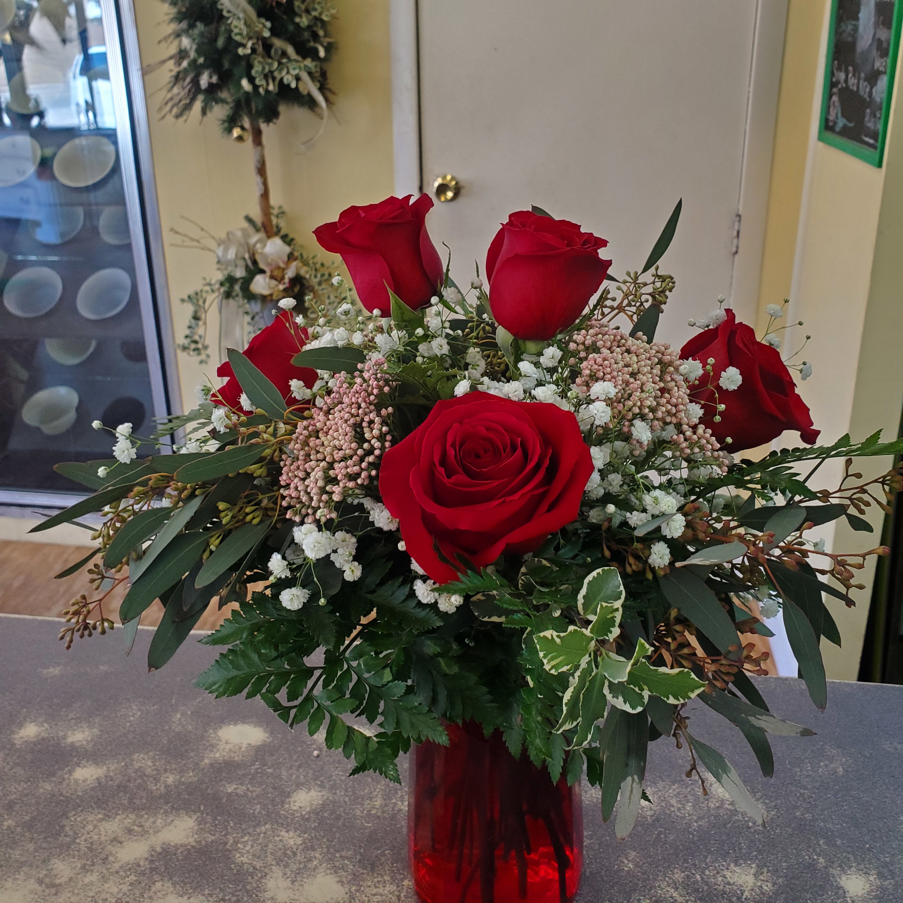Red roses arranged in a red glass vase with white filler flowers