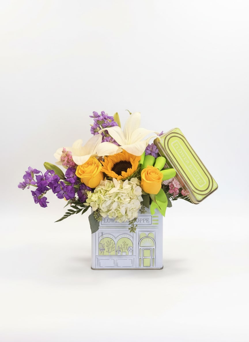 Bouquet of yellow roses, white lilies, and purple flowers in a decorative tin