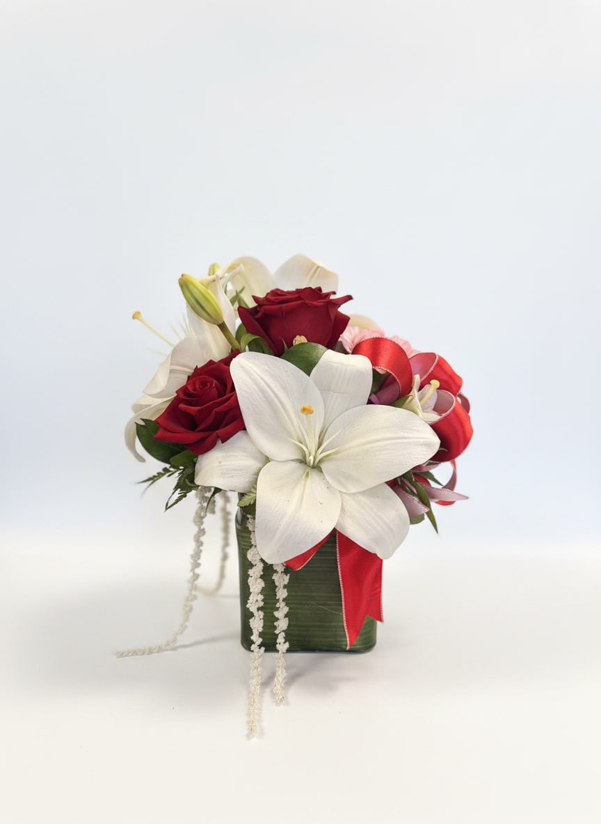 Red roses and white lilies in a green vase with a red ribbon