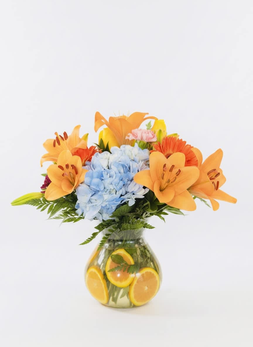 Orange lilies and blue hydrangeas in a glass vase with sliced oranges