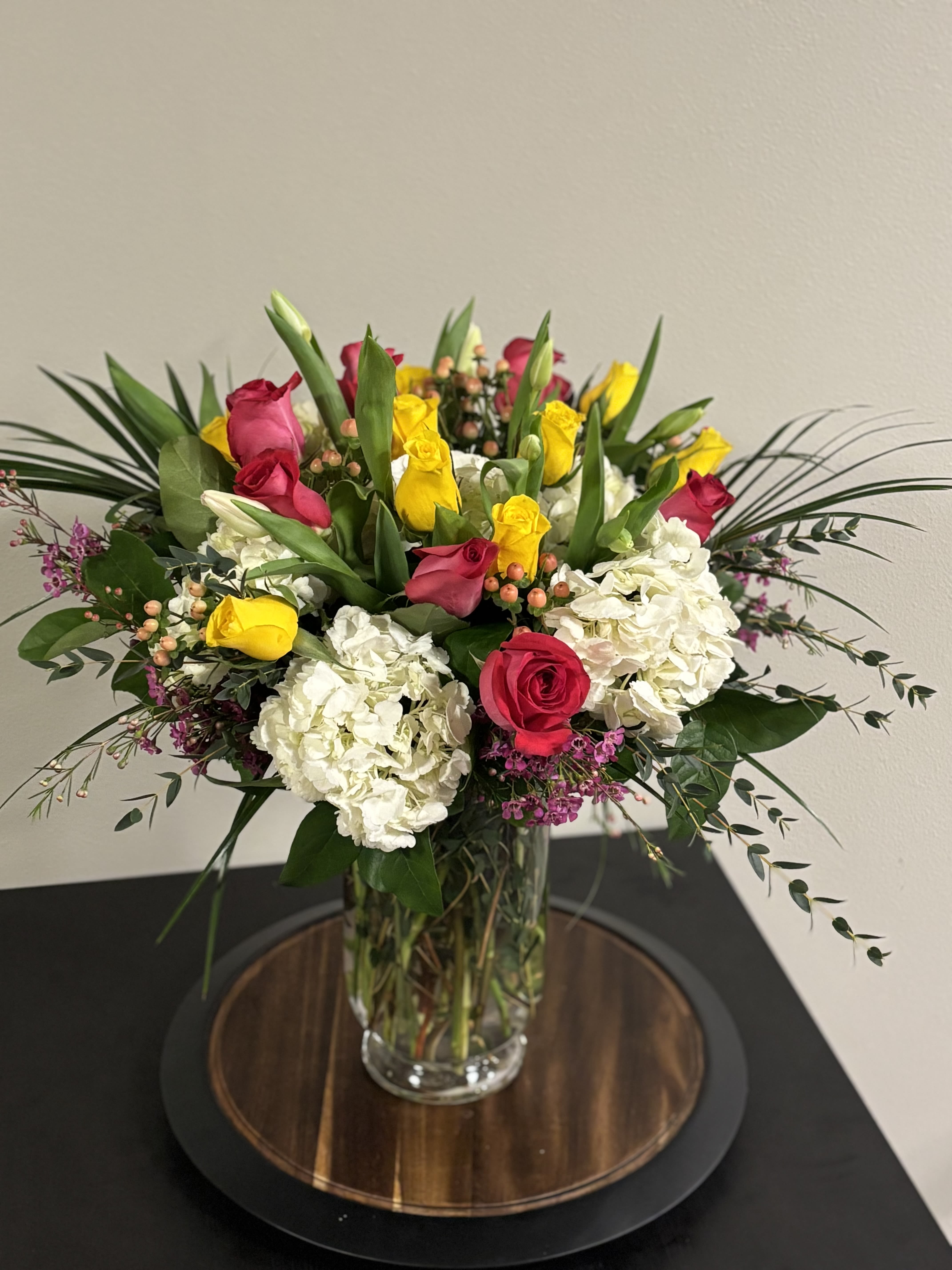 Bouquet of pink and yellow roses with white hydrangeas in a clear glass vase
