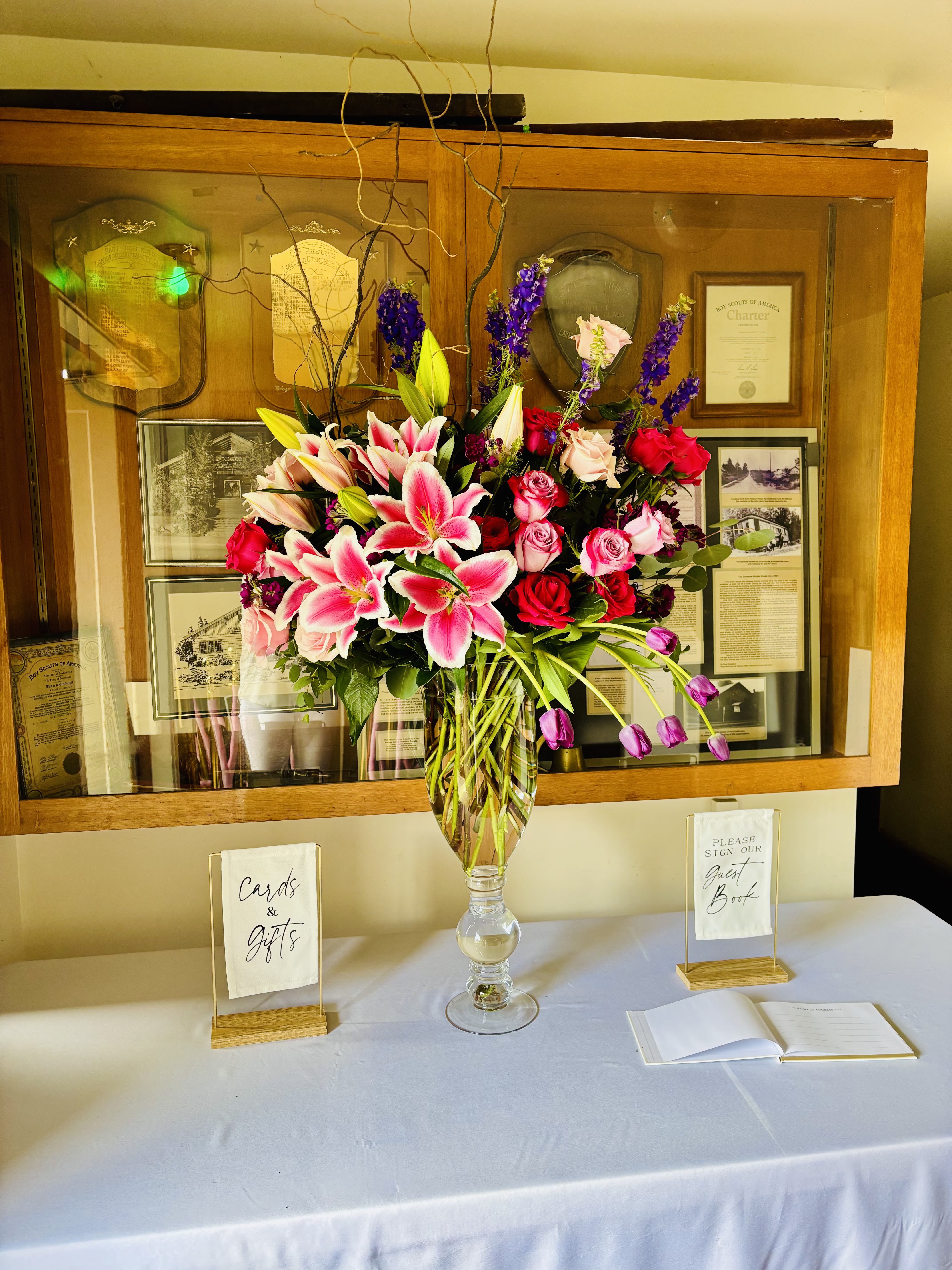 Tall vase arrangement with pink lilies and red roses on a table