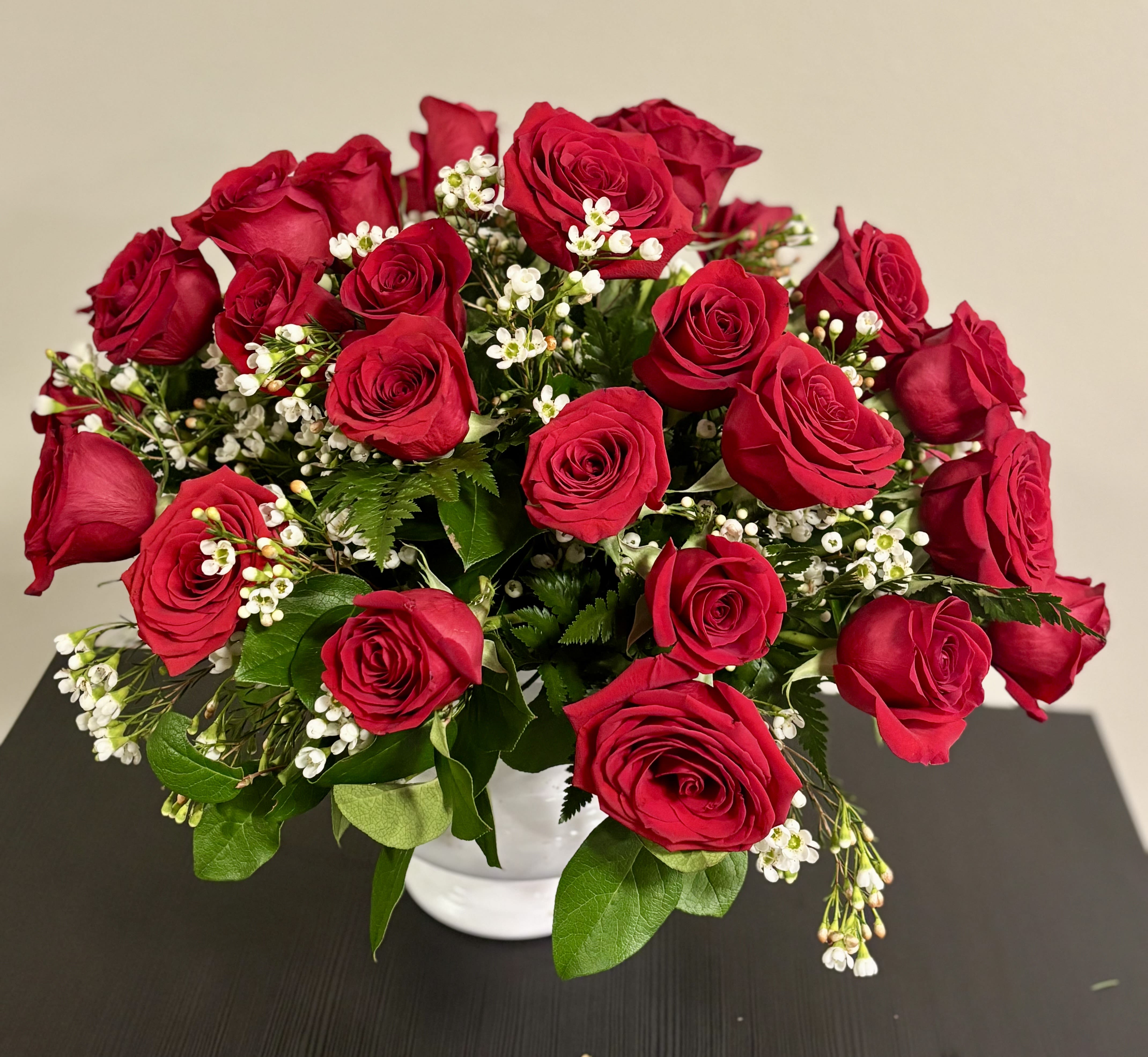 Bouquet of red roses with small white filler flowers in a white vase