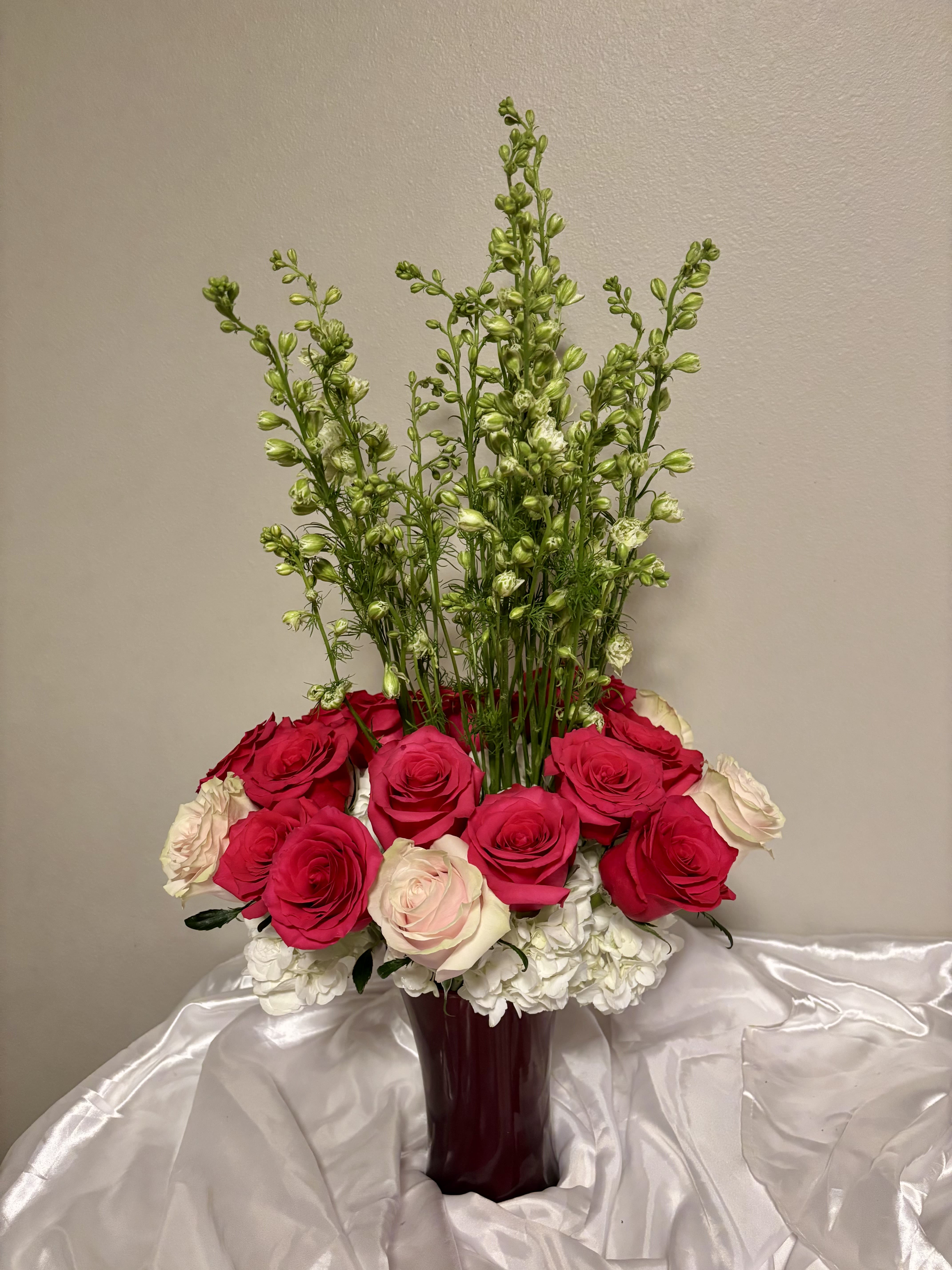 Tall bouquet of red, pink, and white roses in a burgundy vase