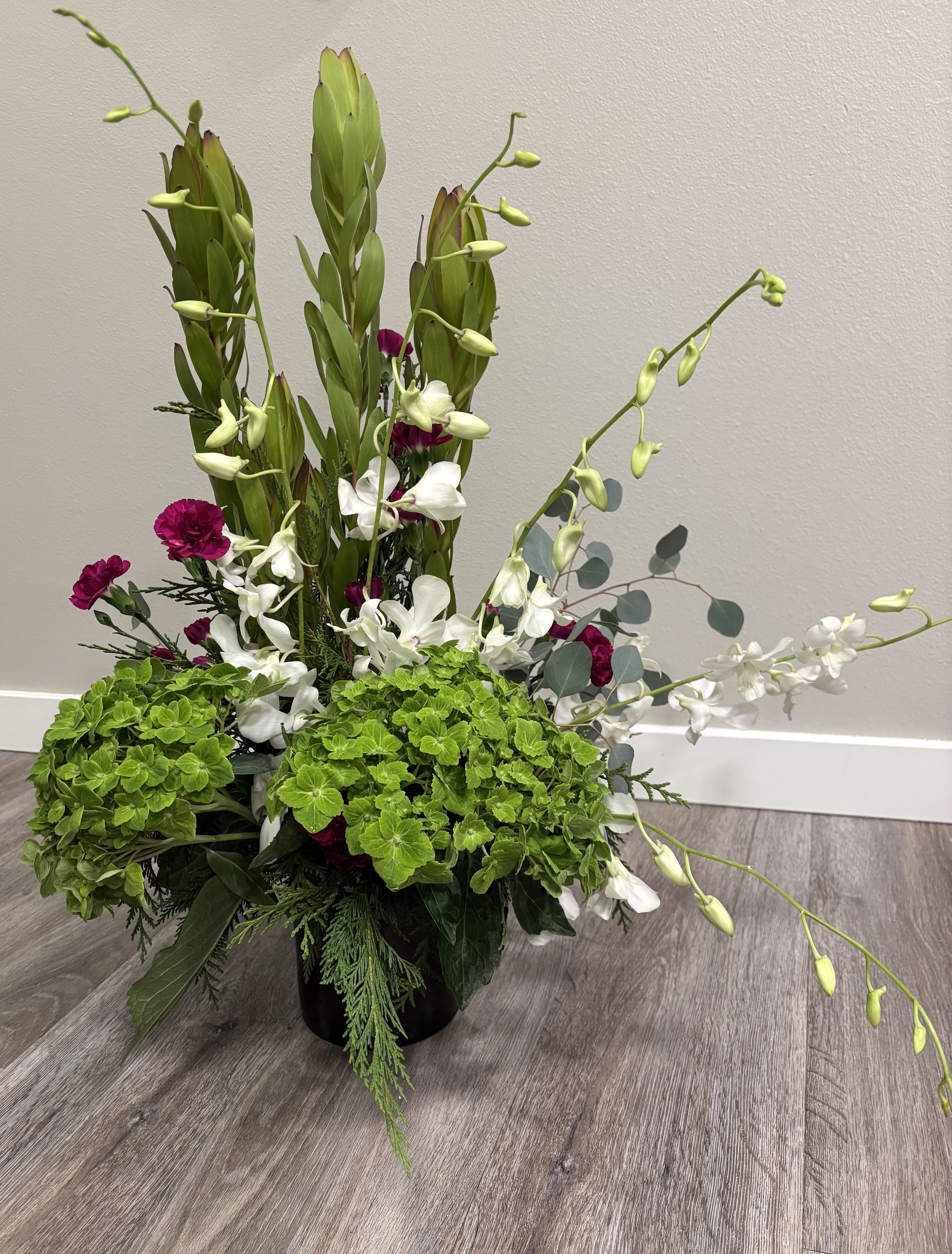Tall floral arrangement with white orchids, magenta carnations, and green hydrangeas in a black vase