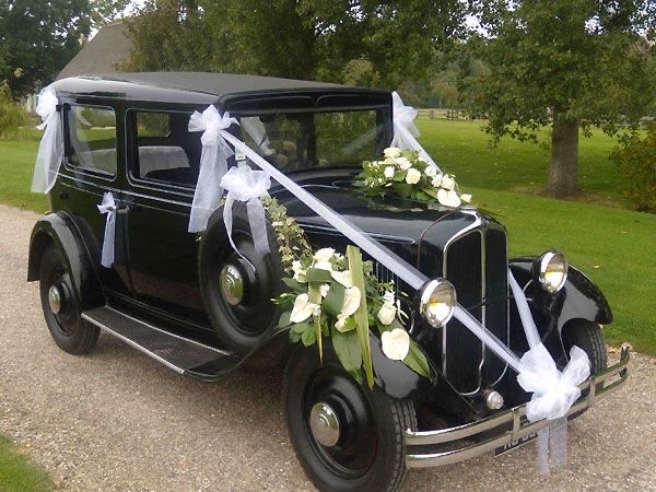 Black vintage car decorated with white ribbons and floral sprays