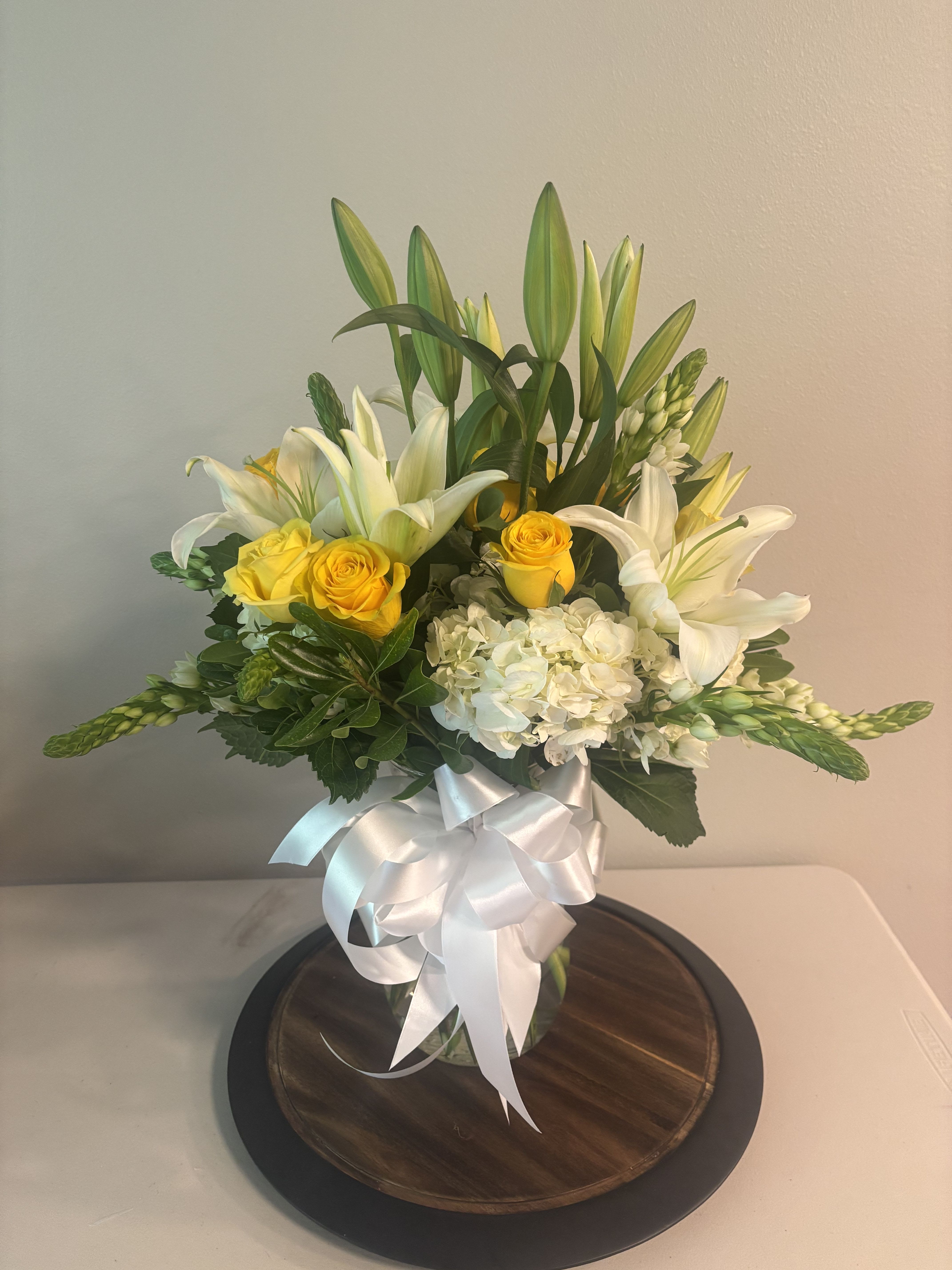 Bouquet of white lilies, yellow roses, and white hydrangeas in a glass vase with a white ribbon