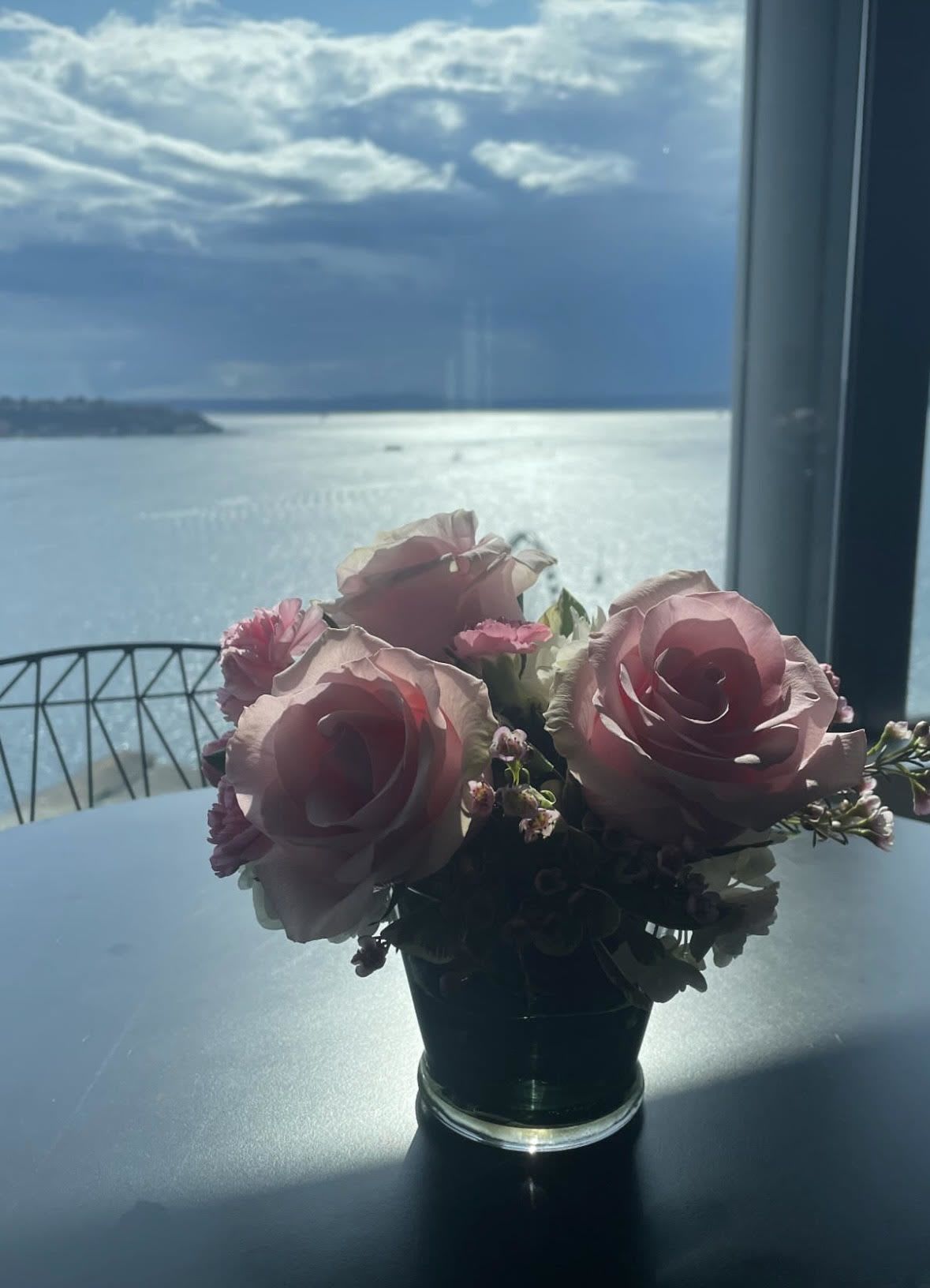 Pink rose bouquet in a small glass vase on a table by a window