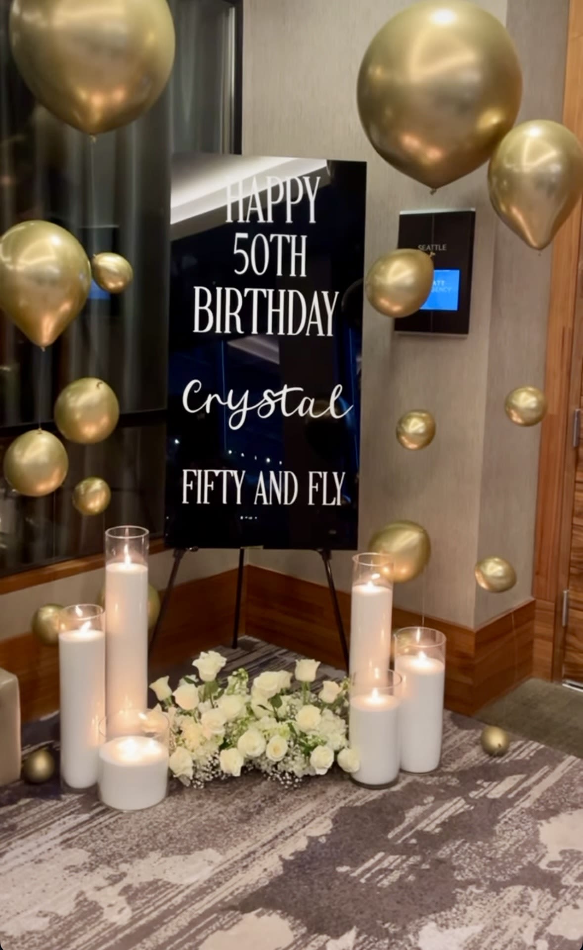 Gold balloons surround a 50th birthday sign with white flowers and candles