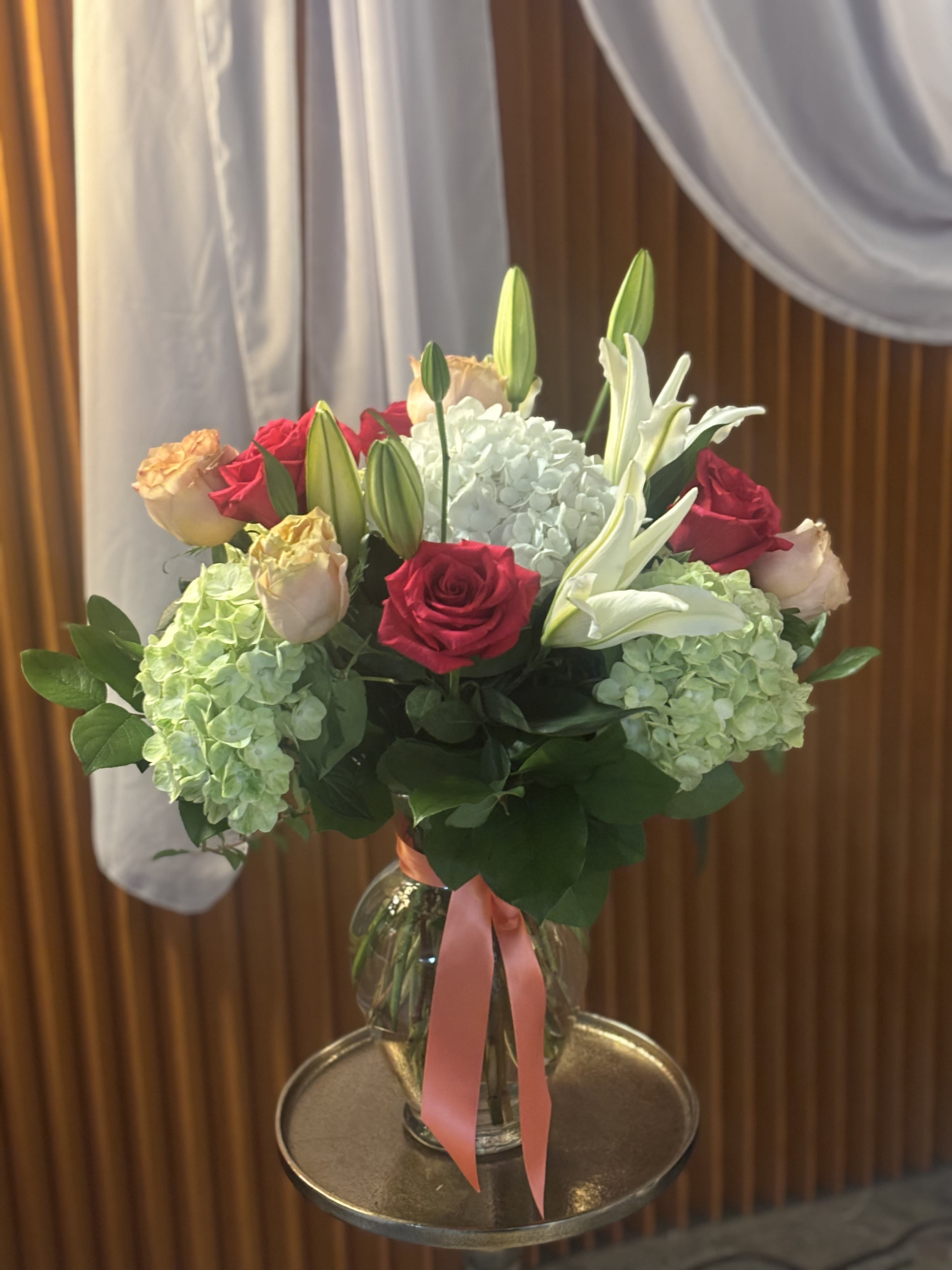 Bouquet of red and peach roses with white lilies and hydrangeas in a glass vase