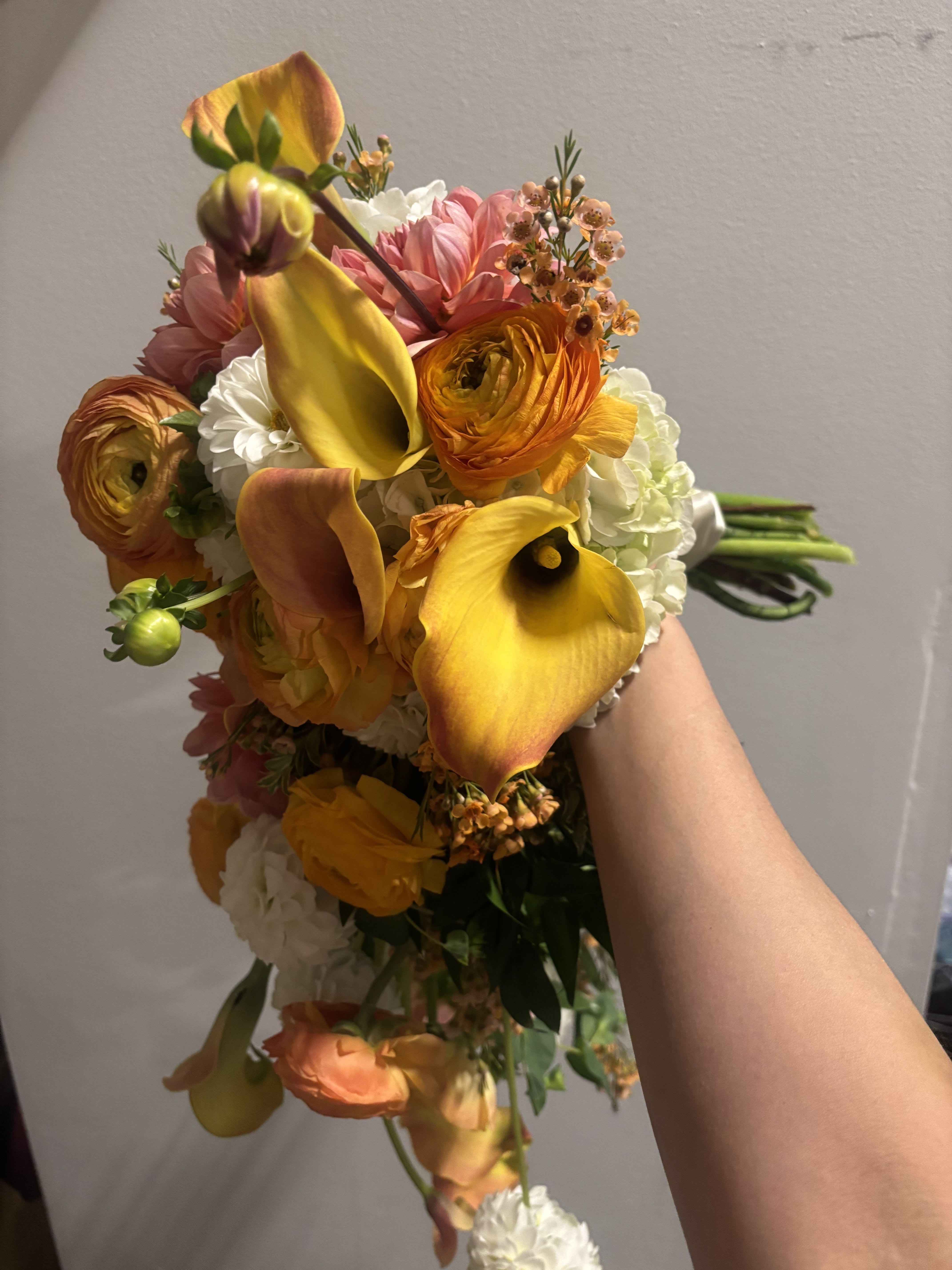 Handheld bouquet with yellow calla lilies, orange ranunculus, and pink blooms