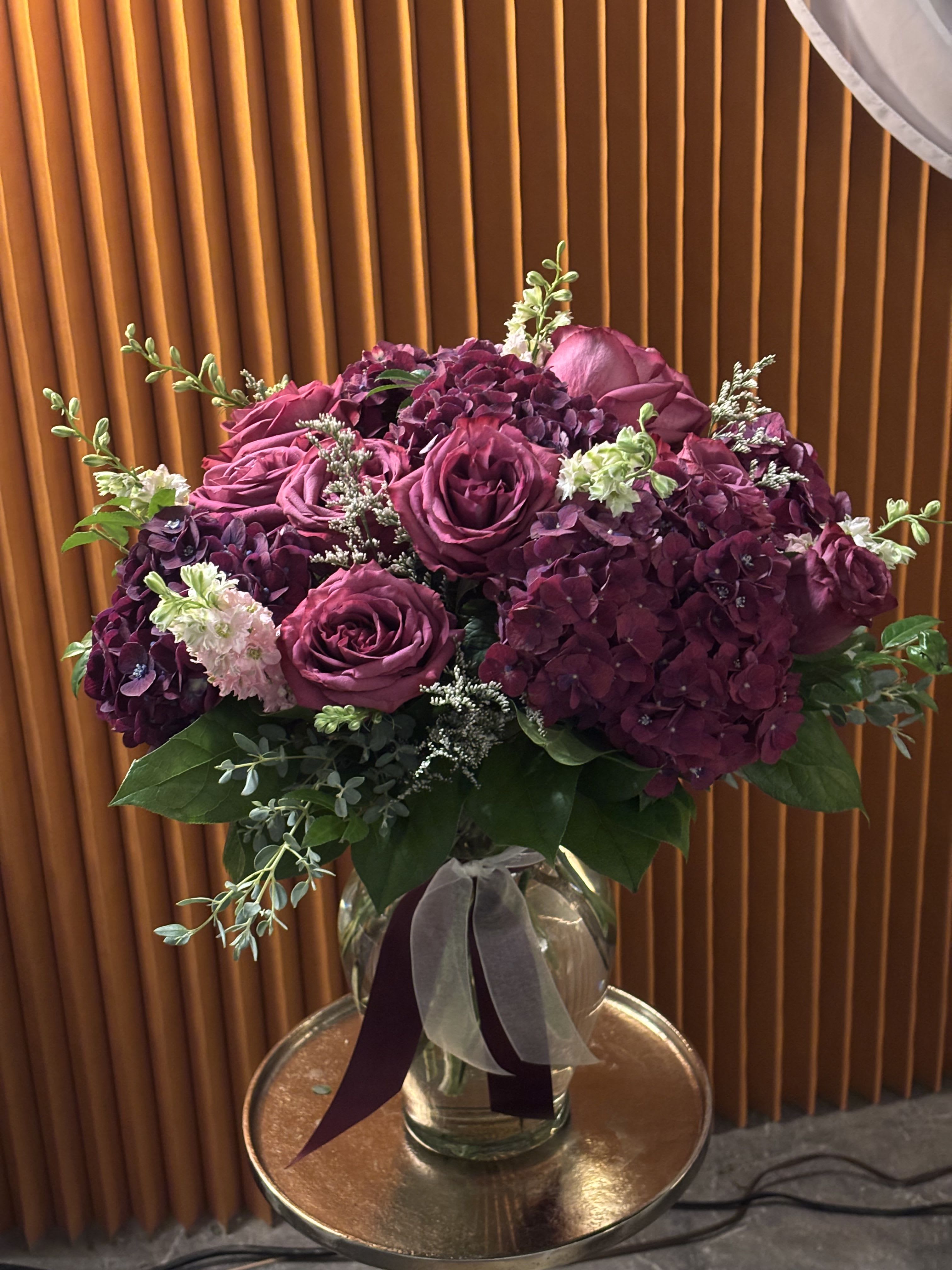 Purple roses and hydrangeas in a glass vase with ribbon