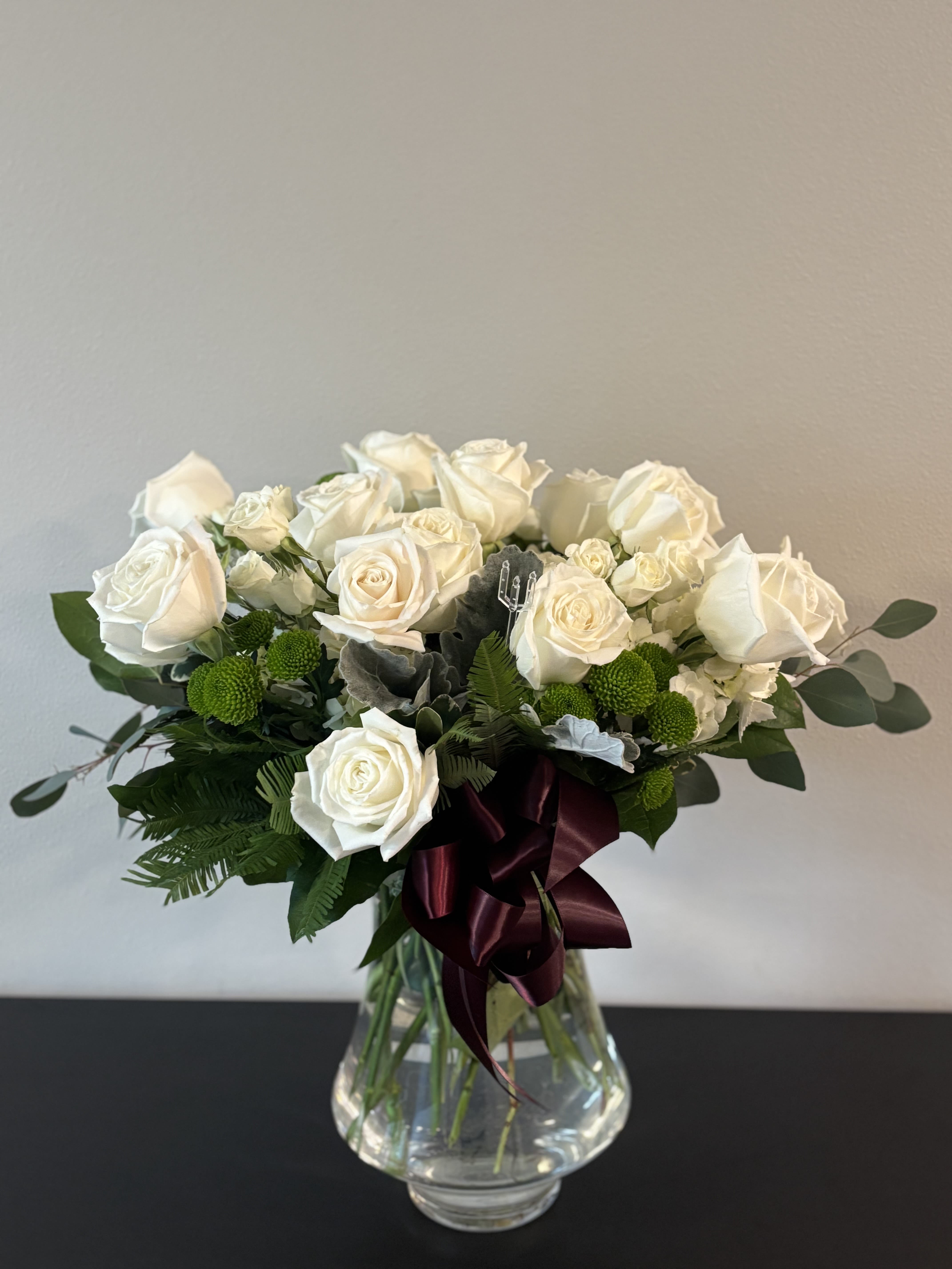 White rose bouquet in a clear glass vase with a burgundy ribbon