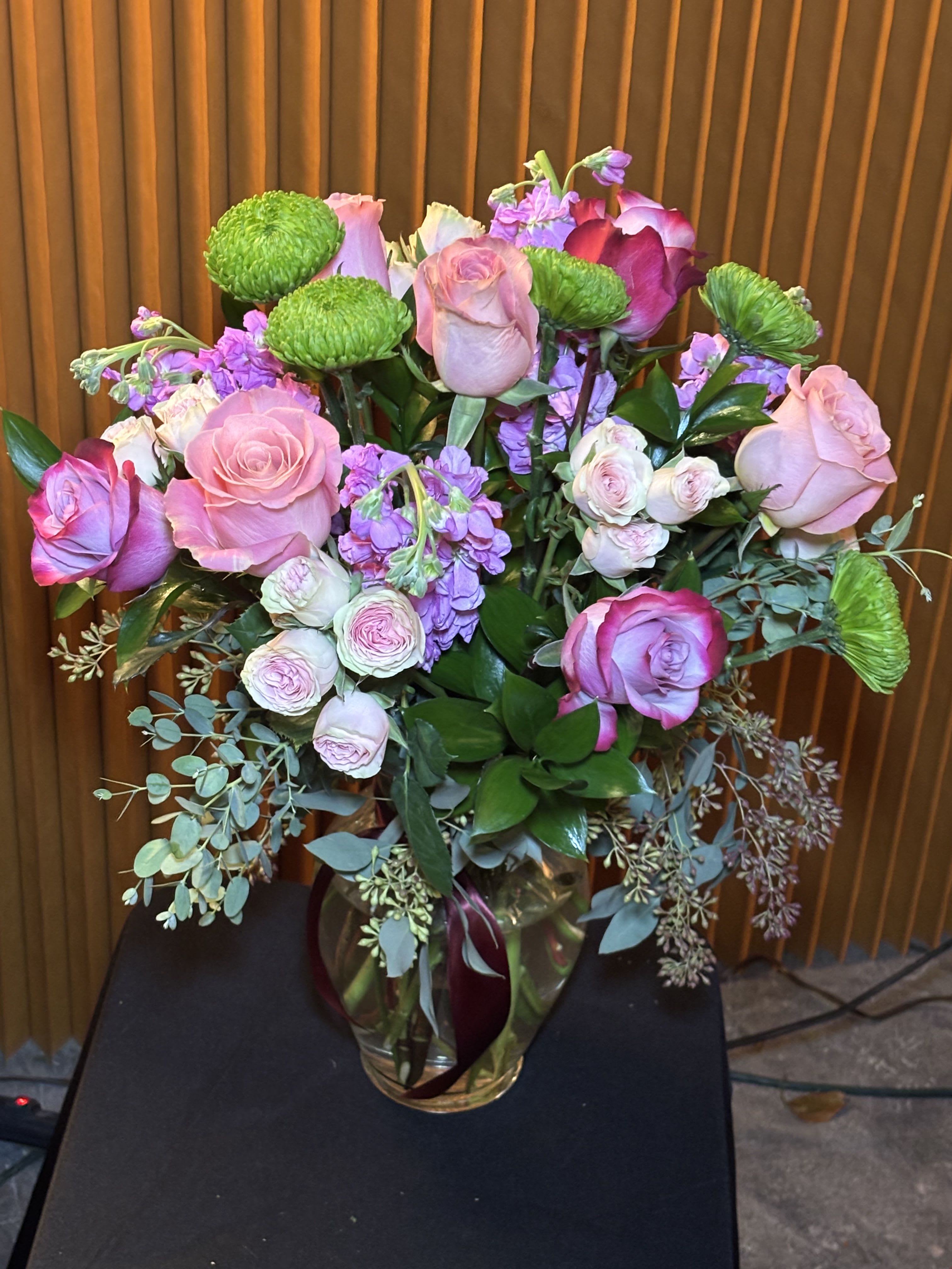 Pink and lavender roses in a glass vase with green button mums