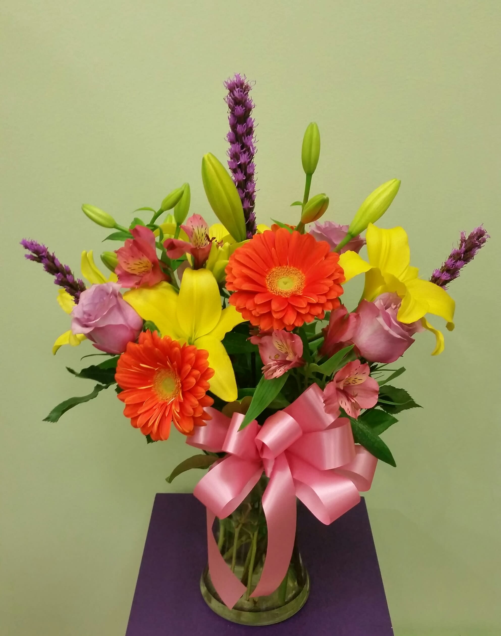 Bouquet of yellow lilies, orange gerberas, and pink roses in a glass vase