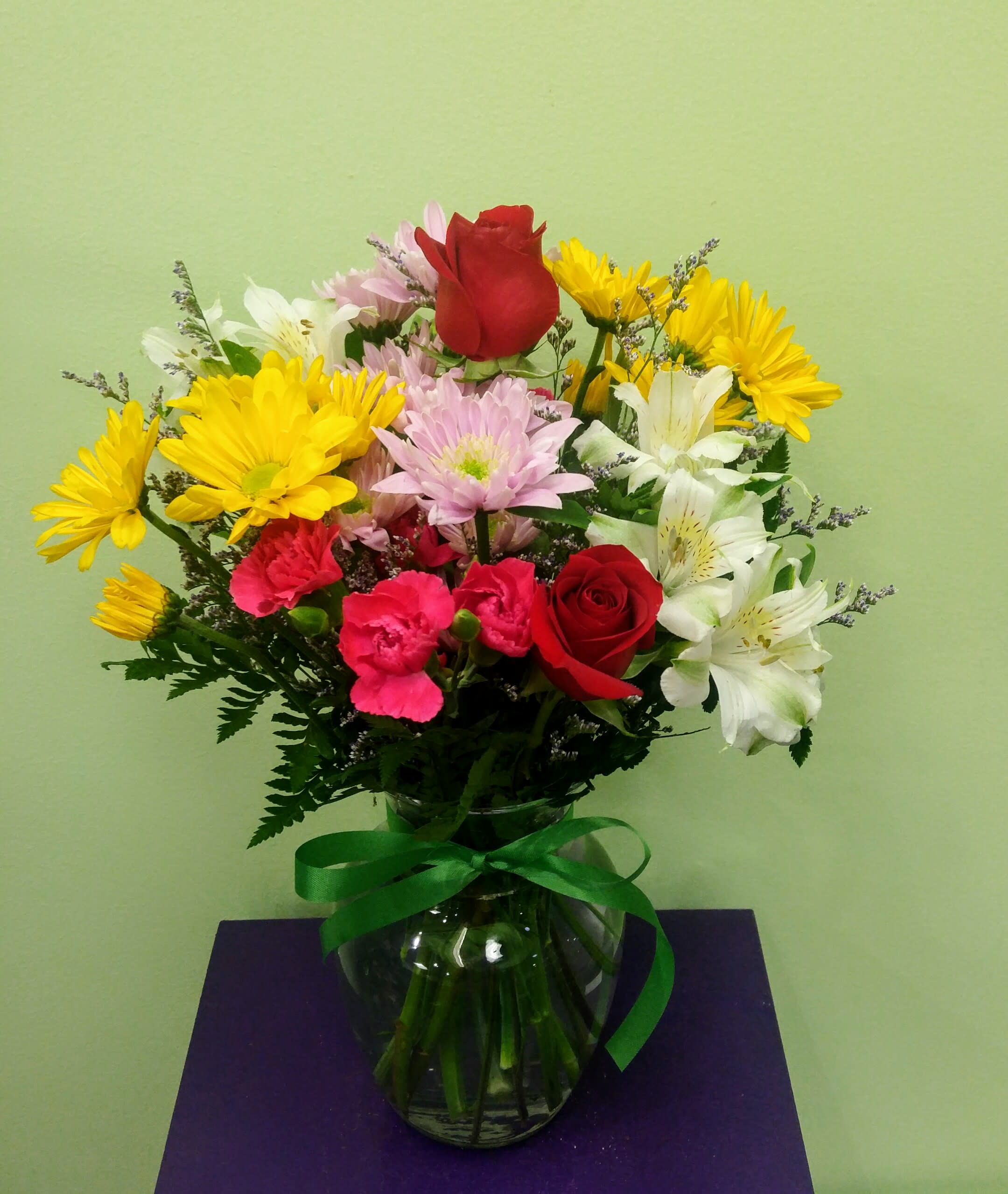 Mixed bouquet of roses, daisies, carnations, and alstroemeria in a glass vase