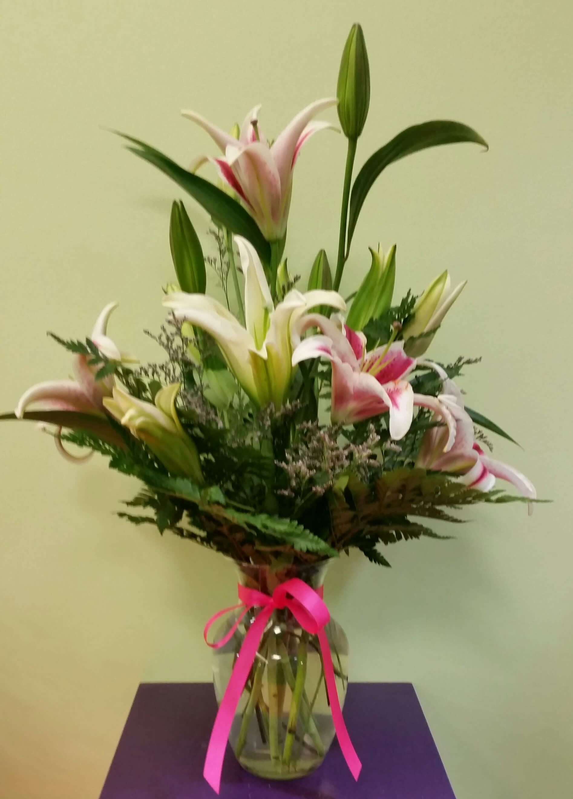 Bouquet of pink and white lilies in a glass vase with a pink ribbon