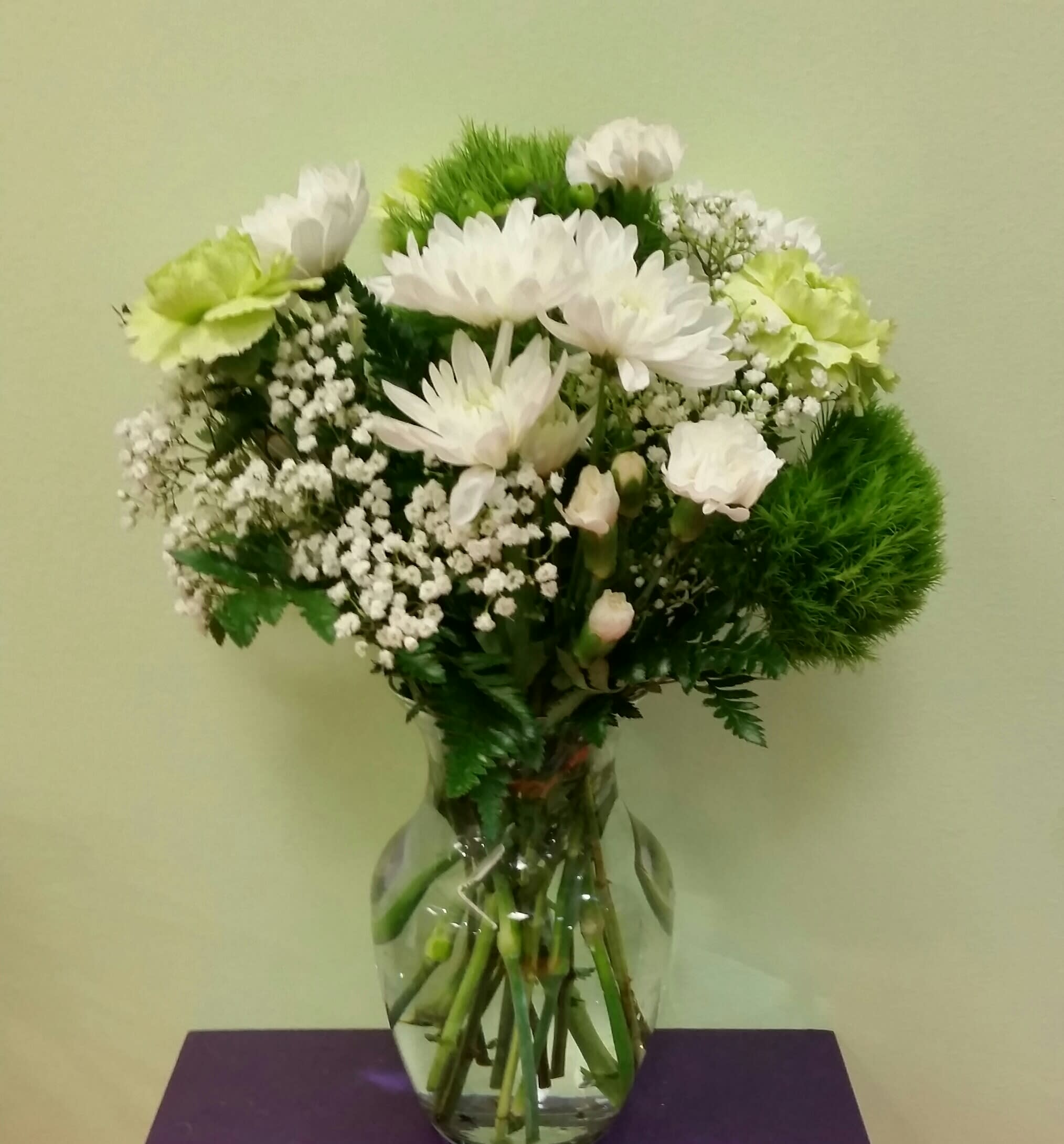 White flowers and green carnations arranged in a clear glass vase